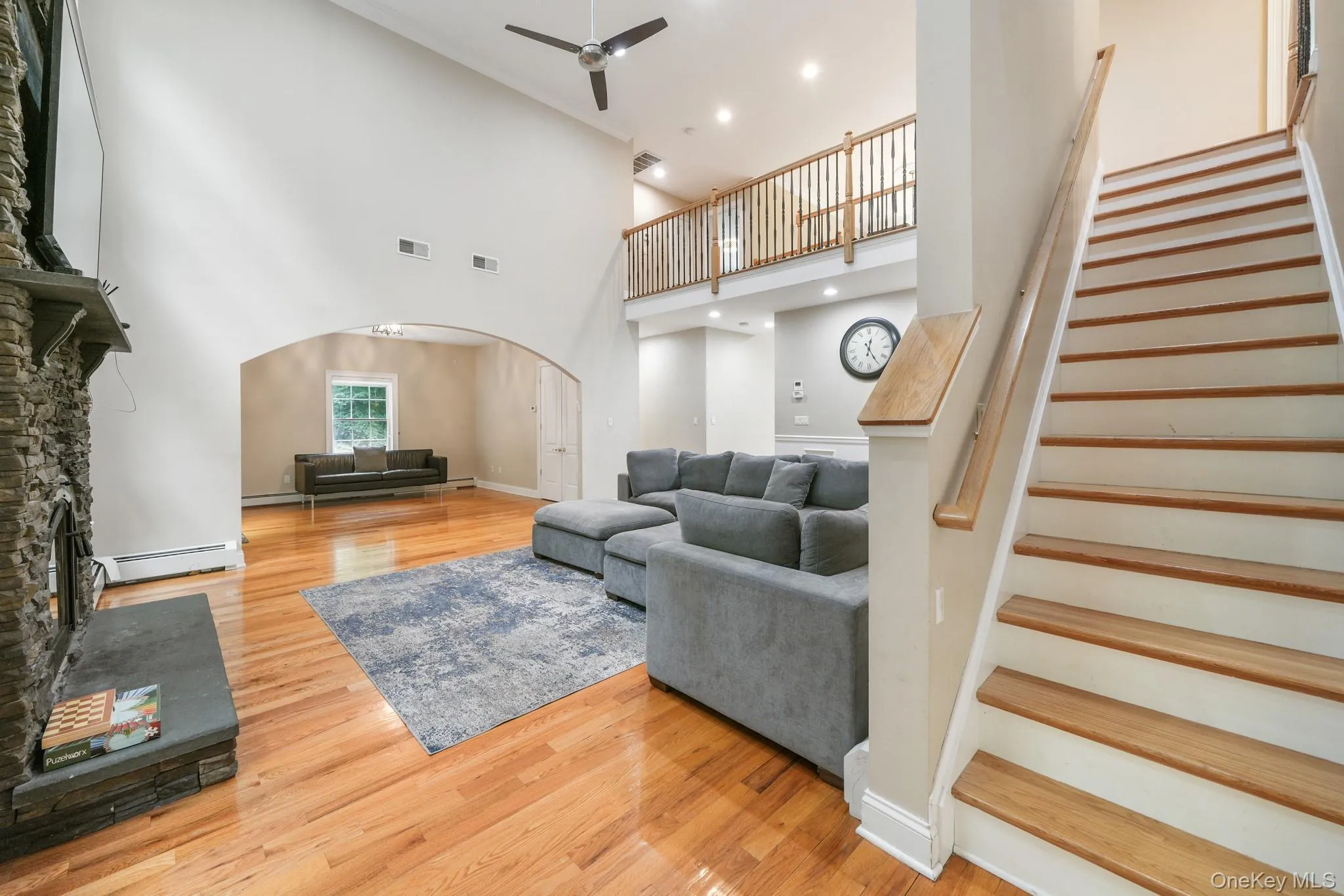 Living room with a stone fireplace, light wood-type flooring, arched walkways, recessed lighting, and a high ceiling Living room with a stone fireplace, light wood-type flooring, arched walkways, recessed lighting, and a high ceiling
