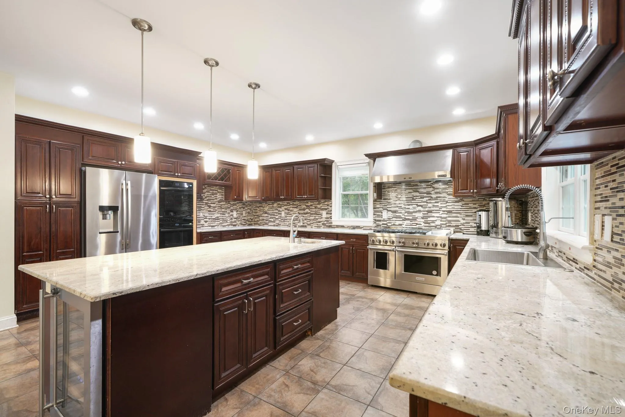 Kitchen featuring hanging light fixtures, an island with sink, light stone counters, stainless steel appliances, and dark brown cabinets Kitchen featuring hanging light fixtures, an island with sink, light stone counters, stainless steel appliances, and dark brown cabinets