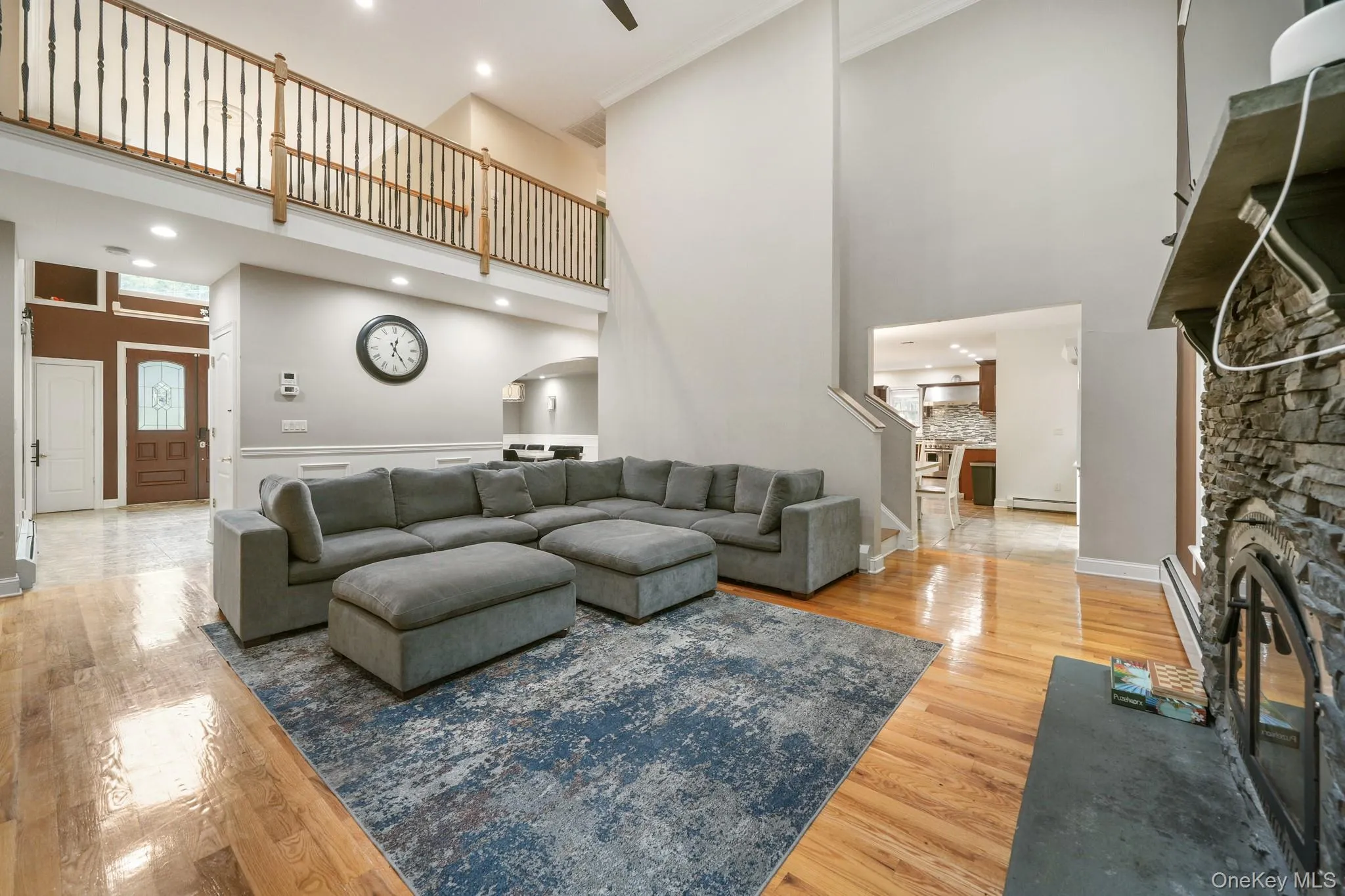 Living area featuring light wood finished floors, a towering ceiling, a stone fireplace, recessed lighting, and baseboard heating Living area featuring light wood finished floors, a towering ceiling, a stone fireplace, recessed lighting, and baseboard heating