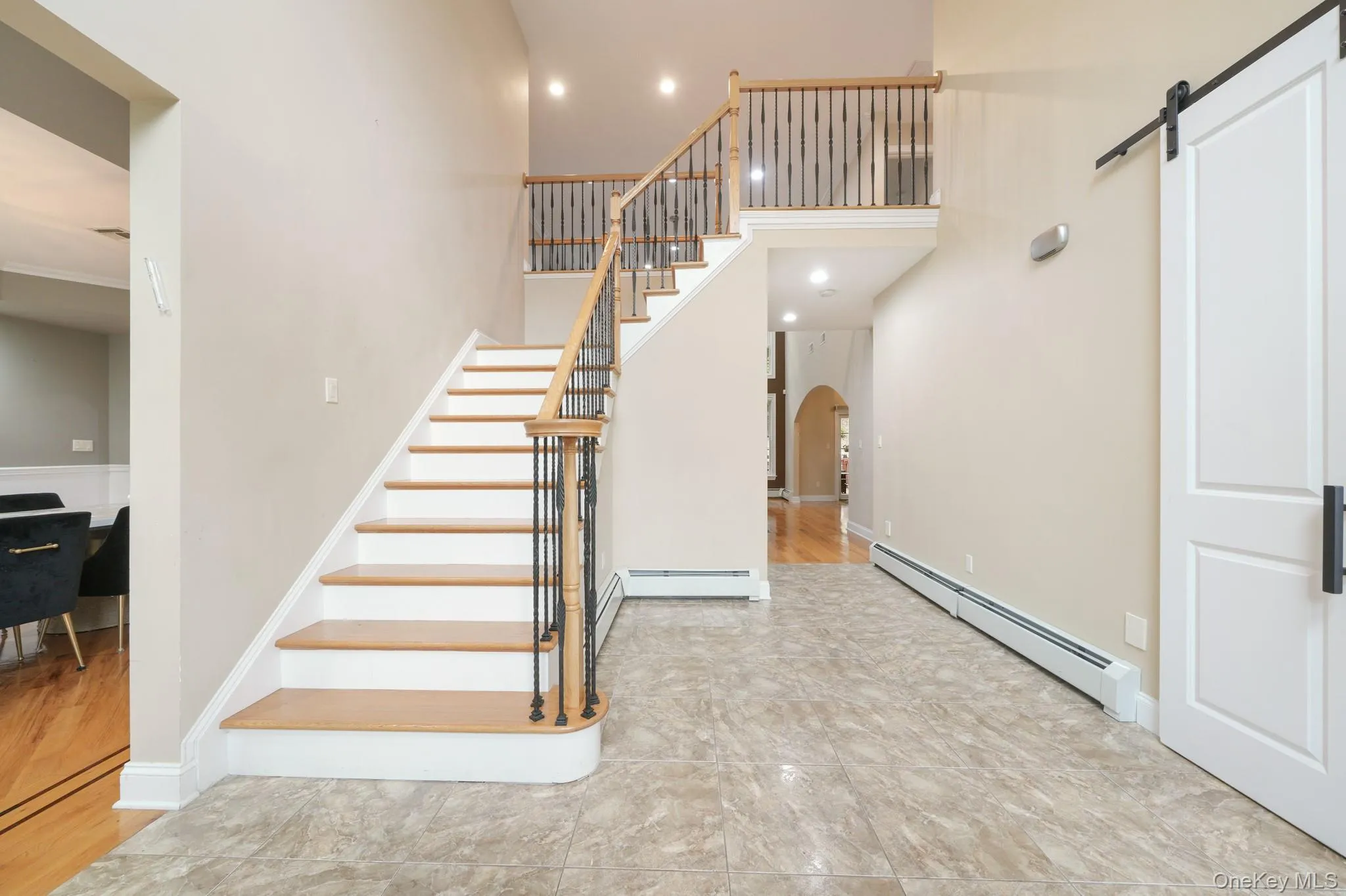 Stairway with a barn door, baseboard heating, arched walkways, a high ceiling, and recessed lighting Stairway with a barn door, baseboard heating, arched walkways, a high ceiling, and recessed lighting