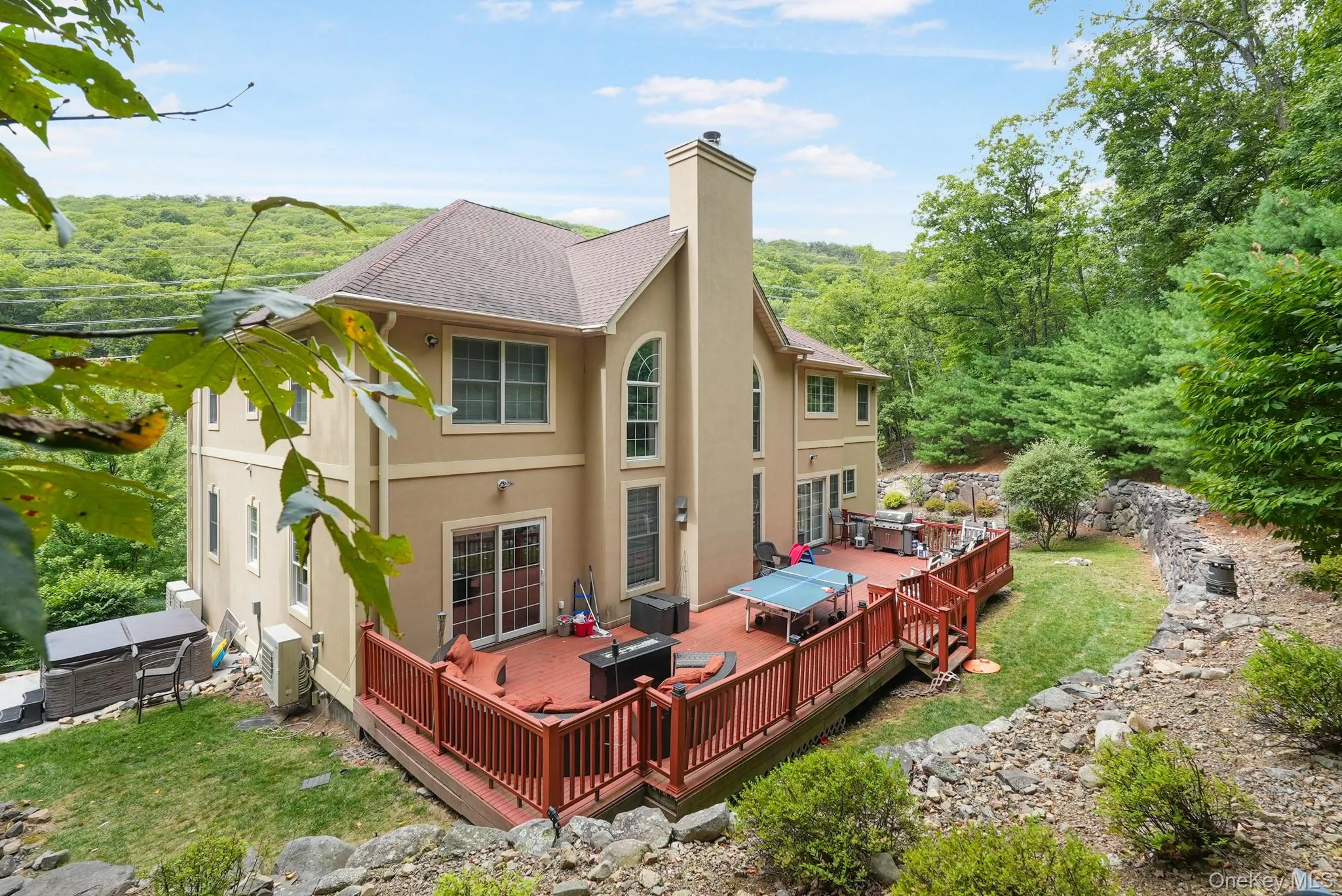 Rear view of house featuring a chimney, a wooden deck, stucco siding, a yard, and a shingled roof Rear view of house featuring a chimney, a wooden deck, stucco siding, a yard, and a shingled roof