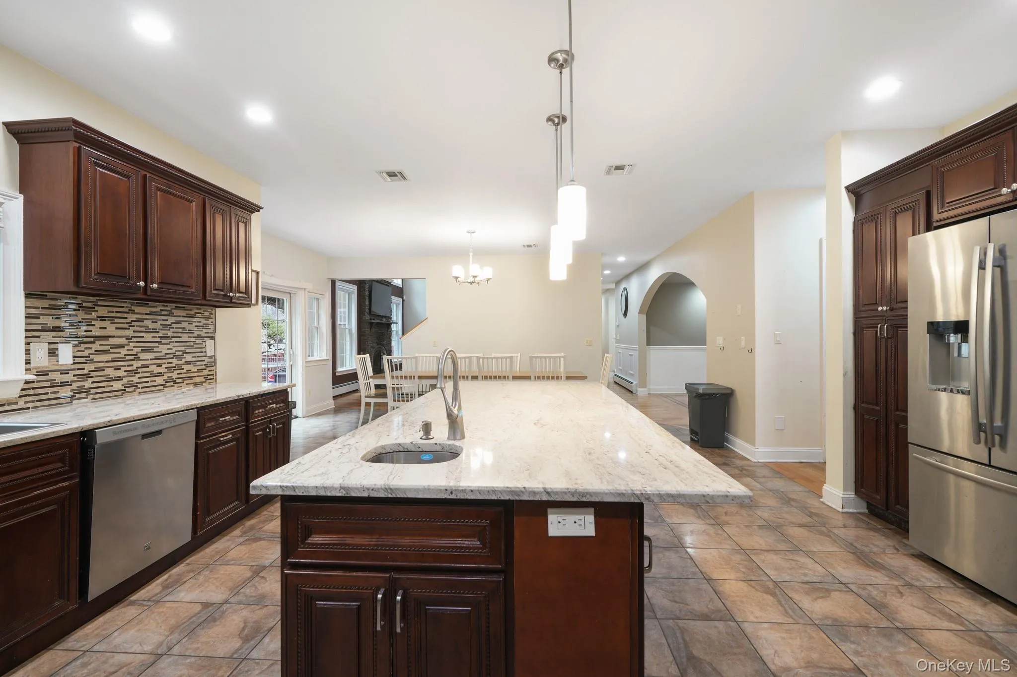 Kitchen featuring dark brown cabinets, appliances with stainless steel finishes, tasteful backsplash, an island with sink, and light stone countertops Kitchen featuring dark brown cabinets, appliances with stainless steel finishes, tasteful backsplash, an island with sink, and light stone countertops