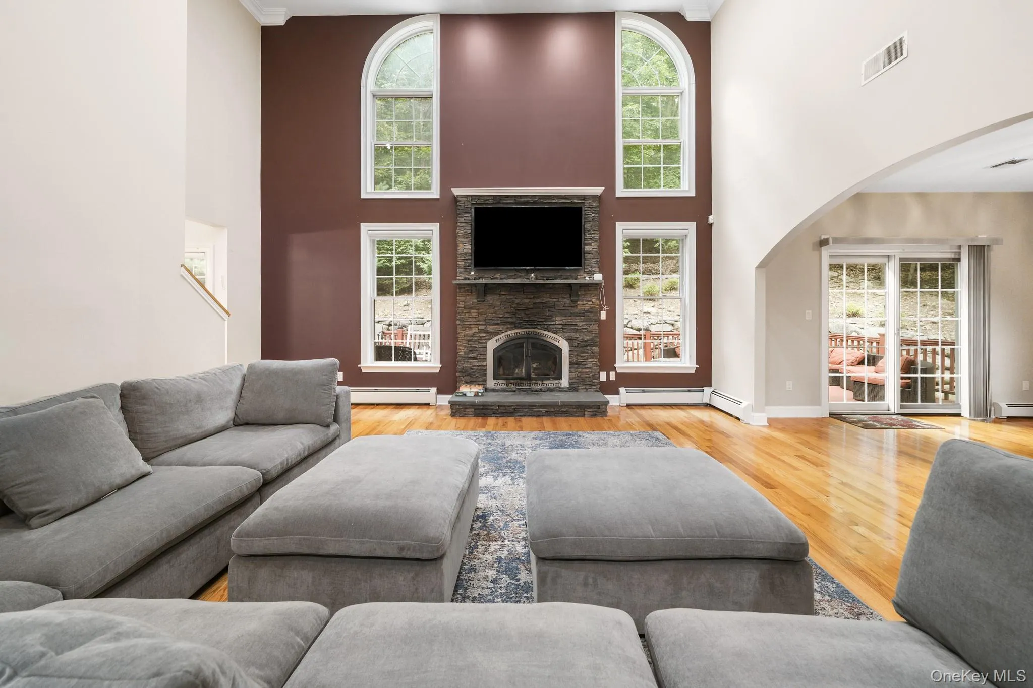 Living room with arched walkways, light wood-type flooring, a high ceiling, a fireplace, and a baseboard radiator Living room with arched walkways, light wood-type flooring, a high ceiling, a fireplace, and a baseboard radiator
