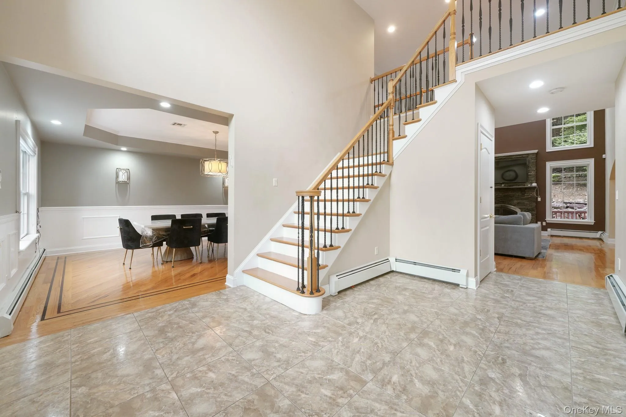 Staircase featuring recessed lighting, a high ceiling, wood finished floors, a raised ceiling, and baseboard heating Staircase featuring recessed lighting, a high ceiling, wood finished floors, a raised ceiling, and baseboard heating