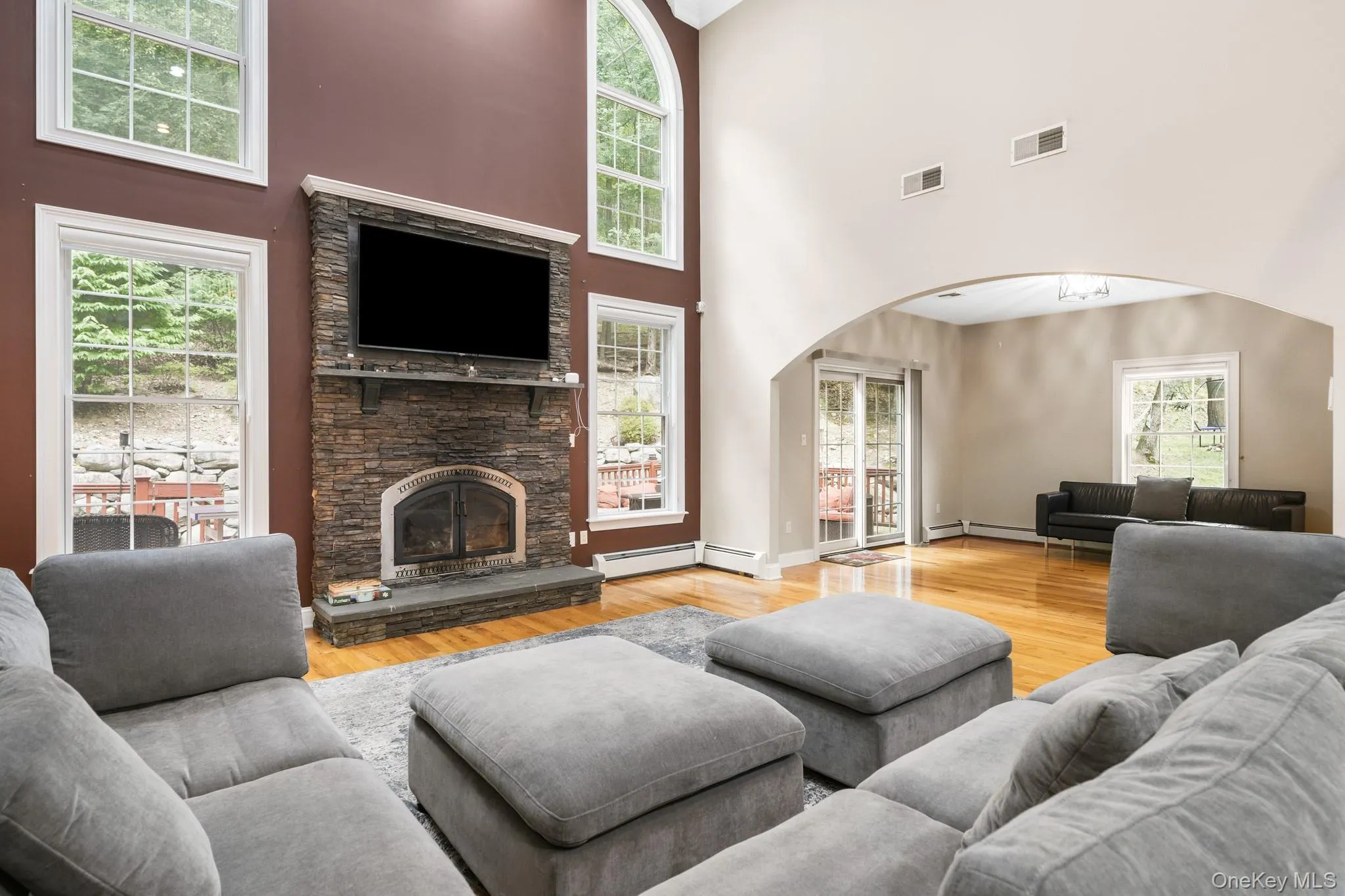 Living area featuring arched walkways, light wood-type flooring, a stone fireplace, and a towering ceiling Living area featuring arched walkways, light wood-type flooring, a stone fireplace, and a towering ceiling