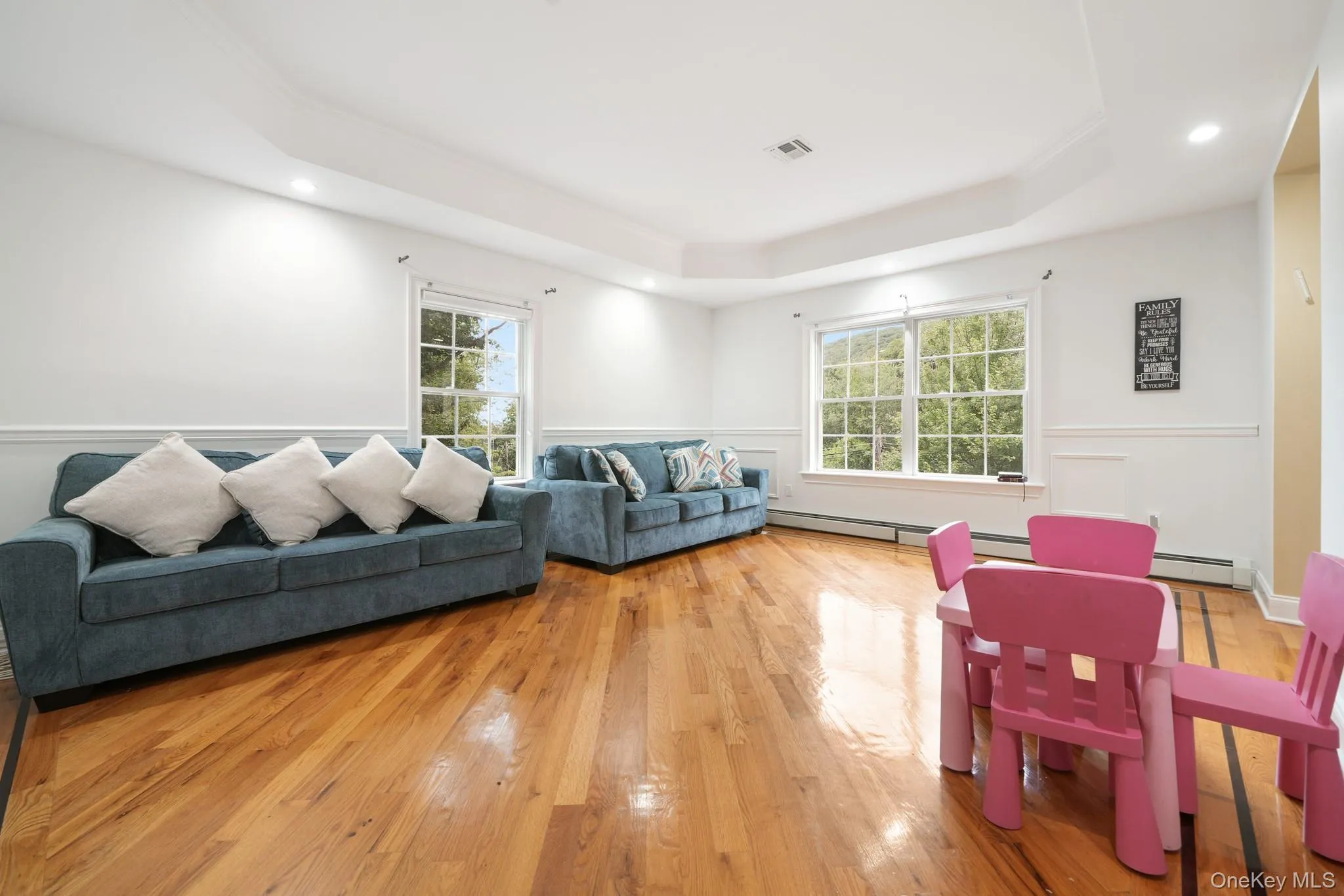 Living area featuring a raised ceiling, light wood-style flooring, recessed lighting, a baseboard heating unit, and wainscoting Living area featuring a raised ceiling, light wood-style flooring, recessed lighting, a baseboard heating unit, and wainscoting