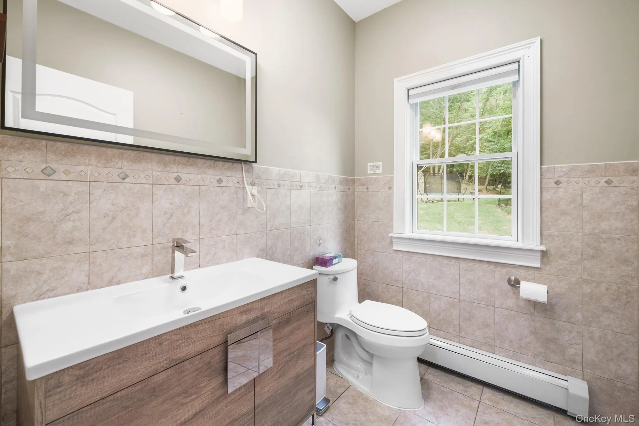 Bathroom with baseboard heating, vanity, light tile patterned flooring, tile walls, and wainscoting Bathroom with baseboard heating, vanity, light tile patterned flooring, tile walls, and wainscoting