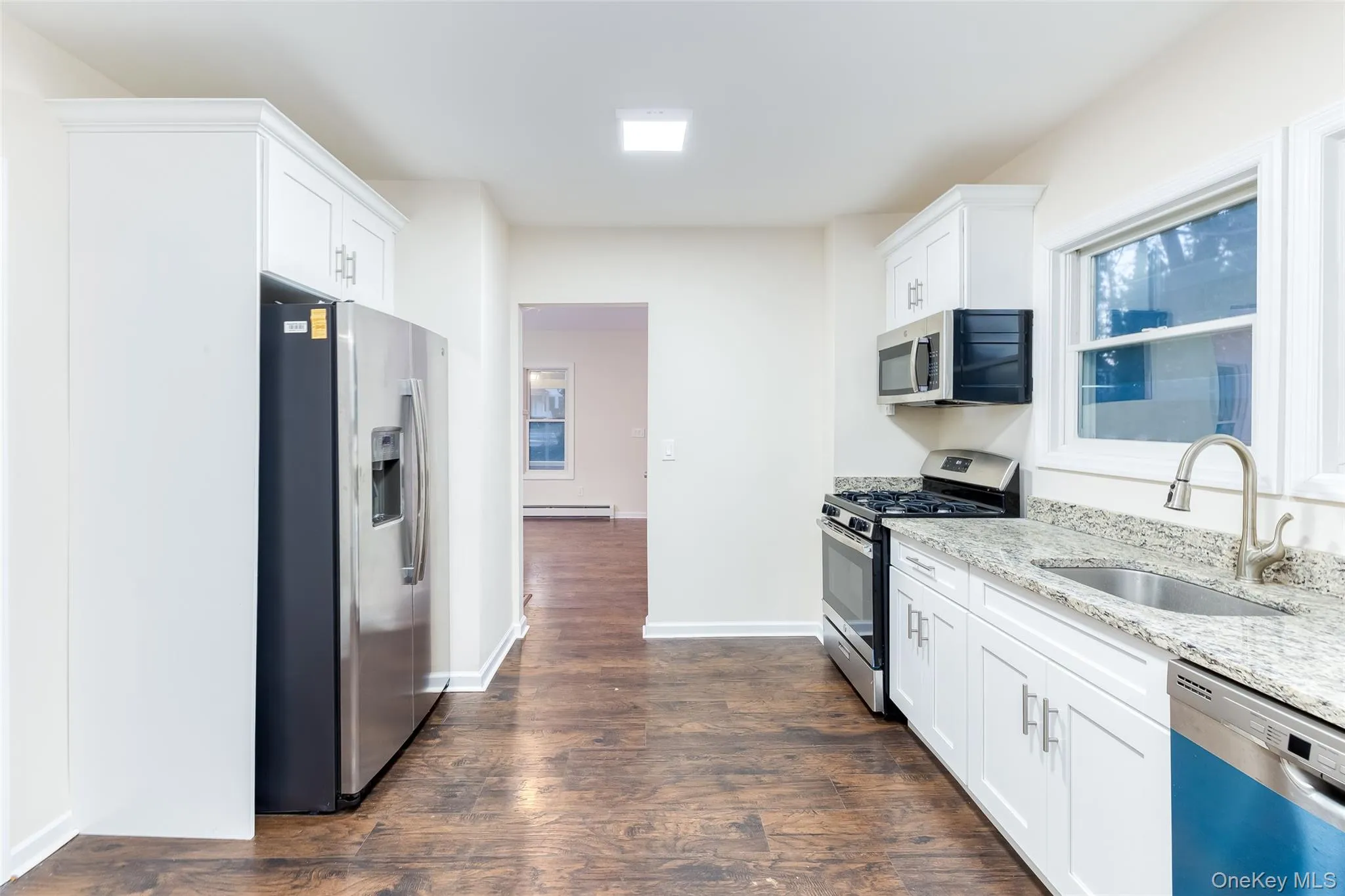 Kitchen featuring appliances with stainless steel finishes, light stone counters, white cabinets, and dark wood-style flooring Kitchen featuring appliances with stainless steel finishes, light stone counters, white cabinets, and dark wood-style flooring