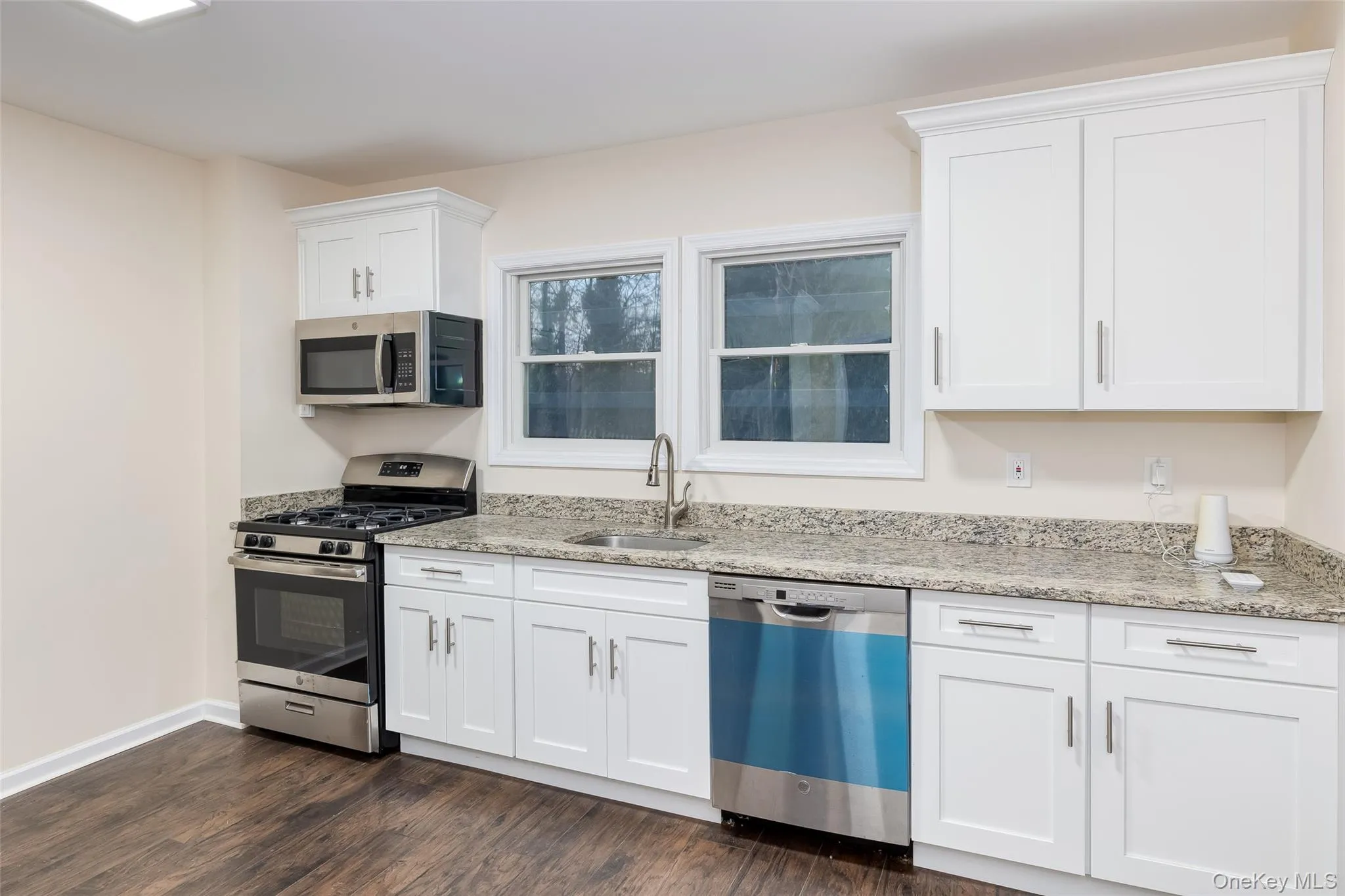 Kitchen featuring stainless steel appliances, white cabinets, light stone countertops, and dark wood finished floors Kitchen featuring stainless steel appliances, white cabinets, light stone countertops, and dark wood finished floors