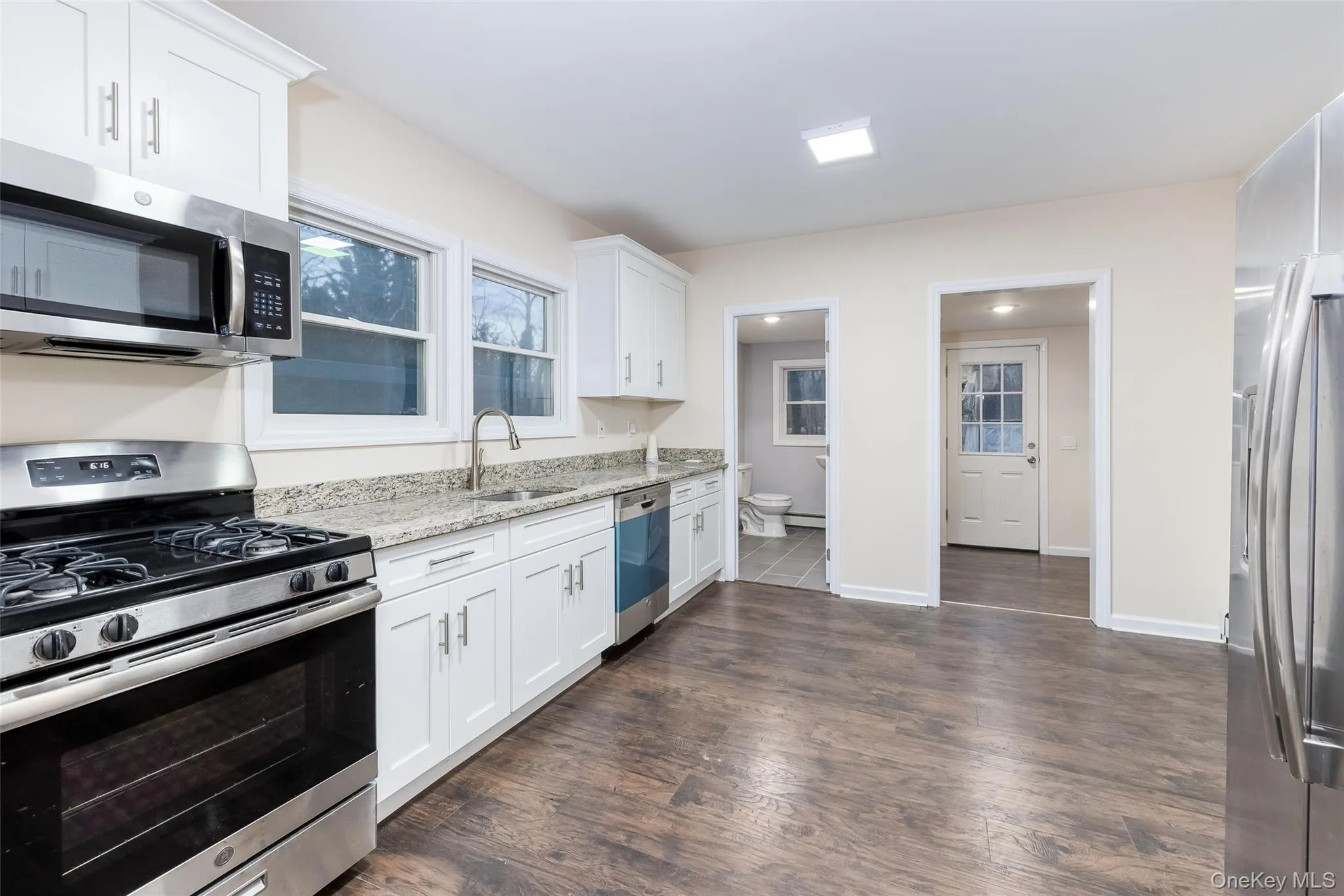 Kitchen featuring stainless steel appliances, light stone counters, white cabinets, and dark wood-style floors Kitchen featuring stainless steel appliances, light stone counters, white cabinets, and dark wood-style floors