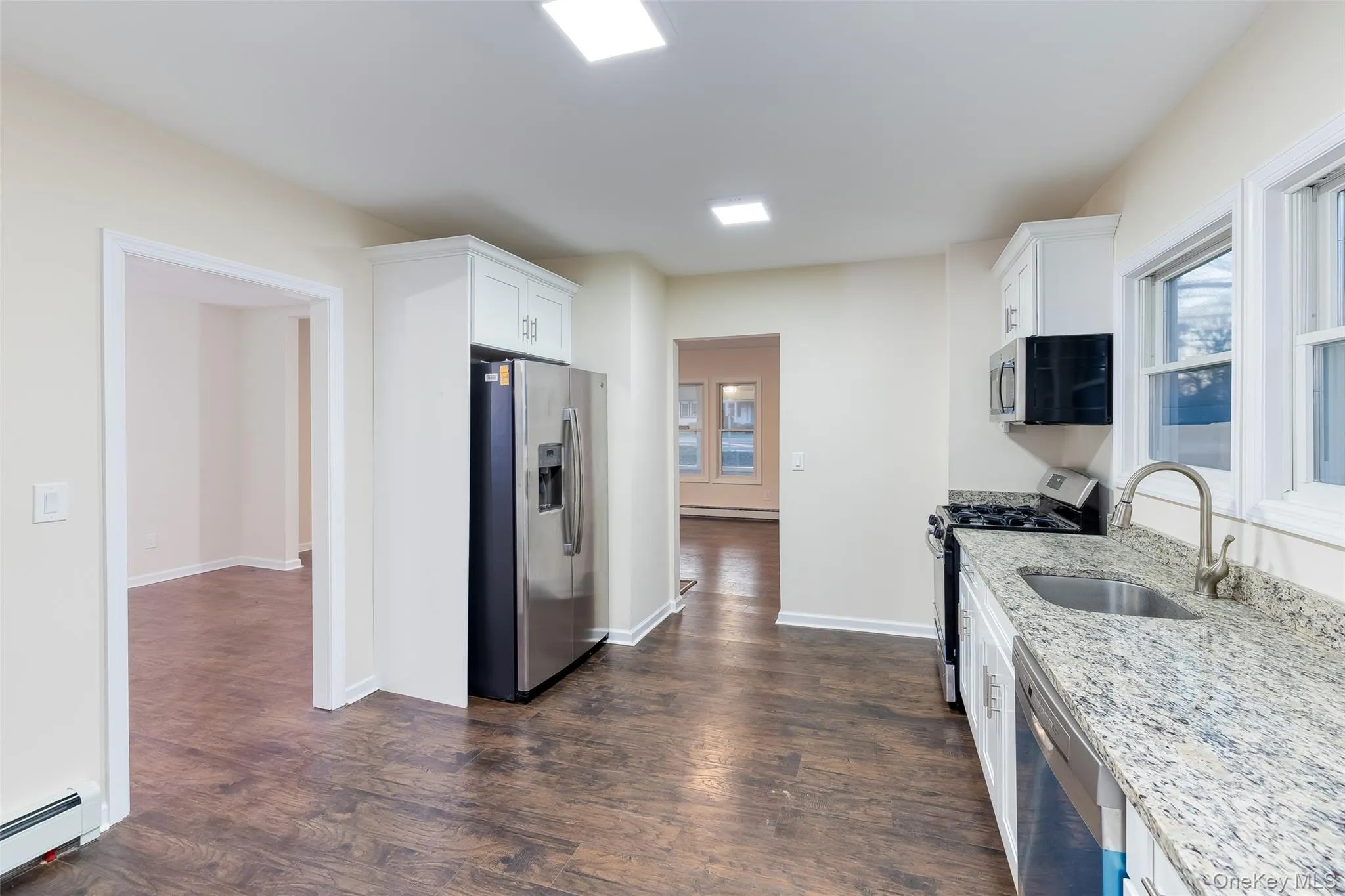 Kitchen featuring stainless steel appliances, light stone countertops, white cabinetry, dark wood-style flooring, and plenty of natural light Kitchen featuring stainless steel appliances, light stone countertops, white cabinetry, dark wood-style flooring, and plenty of natural light