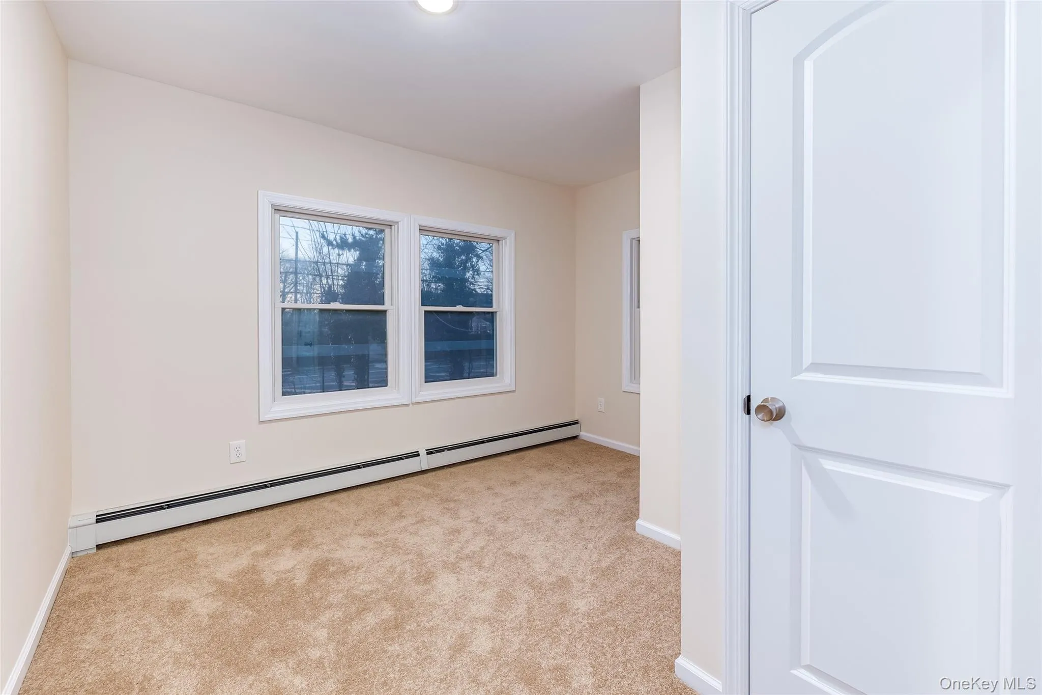 Empty room with a baseboard radiator and light carpet Empty room with a baseboard radiator and light carpet