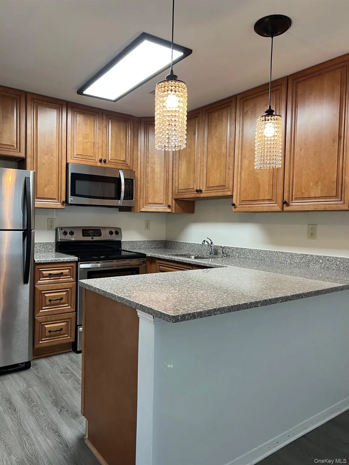 Kitchen with brown cabinets, dark wood finished floors, appliances with stainless steel finishes, and a peninsula Kitchen with brown cabinets, dark wood finished floors, appliances with stainless steel finishes, and a peninsula