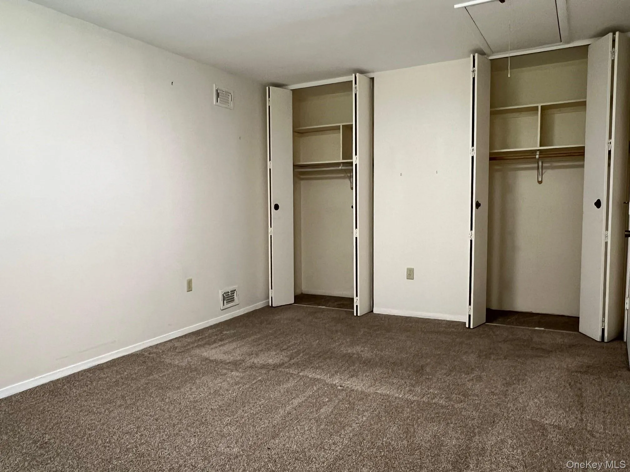 Unfurnished bedroom with multiple closets, dark colored carpet, and attic access Unfurnished bedroom with multiple closets, dark colored carpet, and attic access