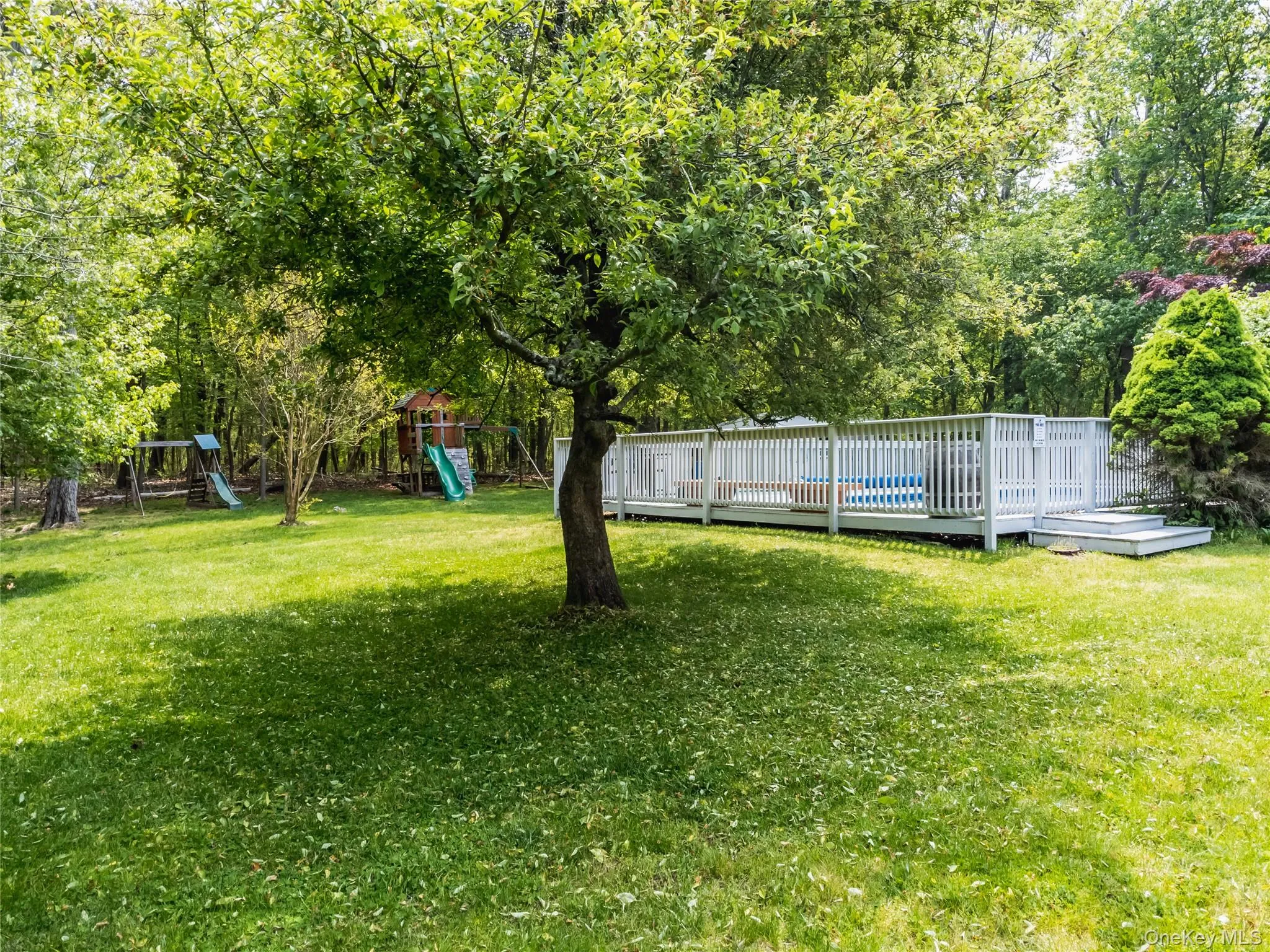 View of grassy yard with a playground, a wooden deck, and view of wooded area View of grassy yard with a playground, a wooden deck, and view of wooded area