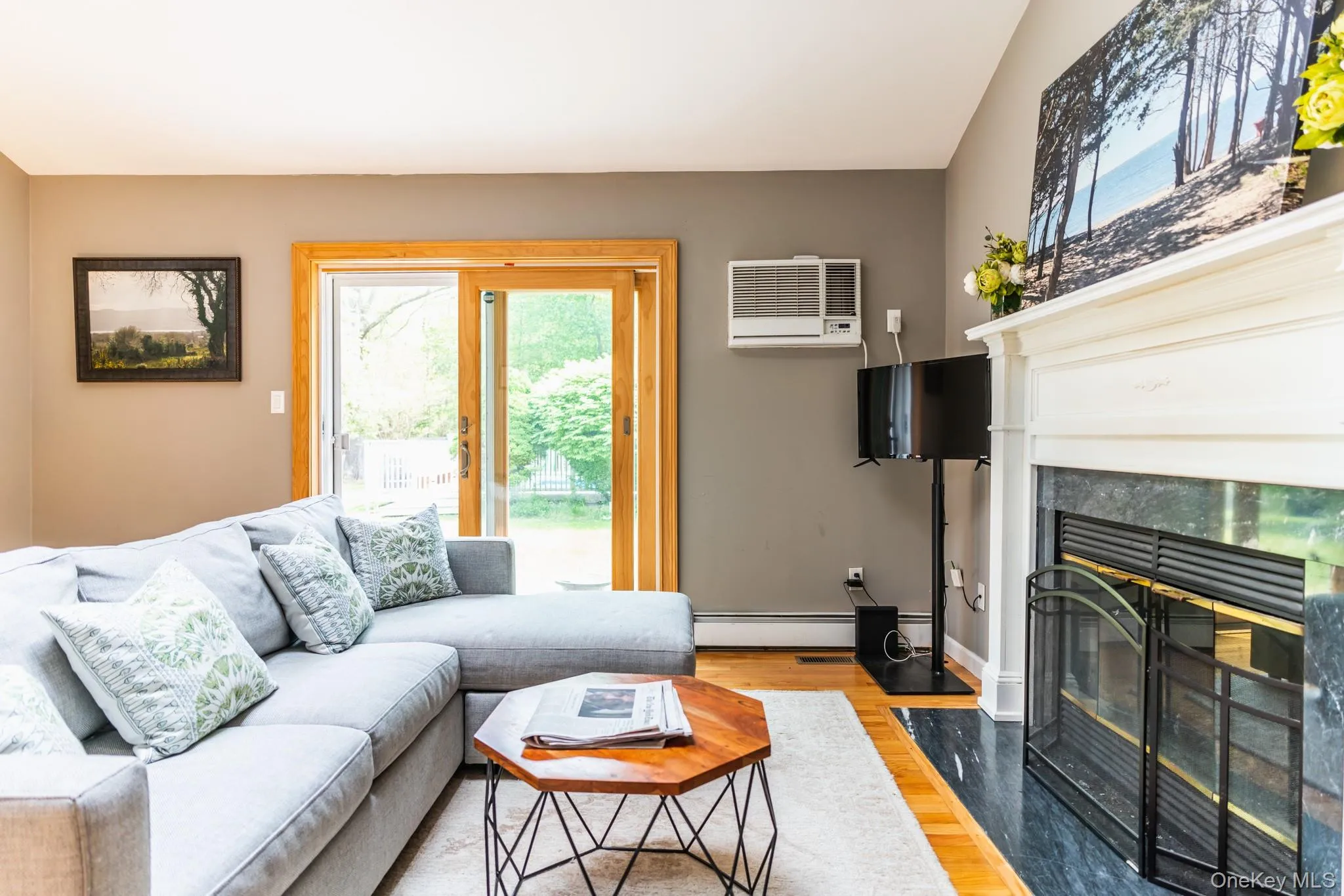 Living room featuring wood finished floors, plenty of natural light, a high end fireplace, and an AC wall unit Living room featuring wood finished floors, plenty of natural light, a high end fireplace, and an AC wall unit