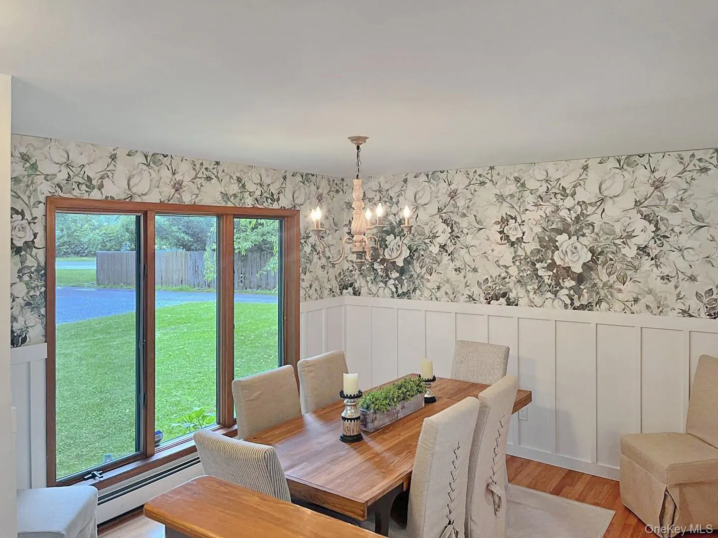 Dining space featuring baseboard heating, a chandelier, wallpapered walls, wood finished floors, and a wainscoted wall Dining space featuring baseboard heating, a chandelier, wallpapered walls, wood finished floors, and a wainscoted wall
