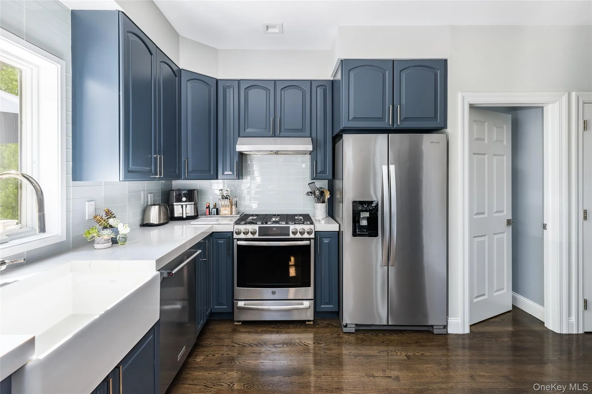 Kitchen featuring blue cabinetry, stainless steel appliances, backsplash, and dark wood-type flooring Kitchen featuring blue cabinetry, stainless steel appliances, backsplash, and dark wood-type flooring
