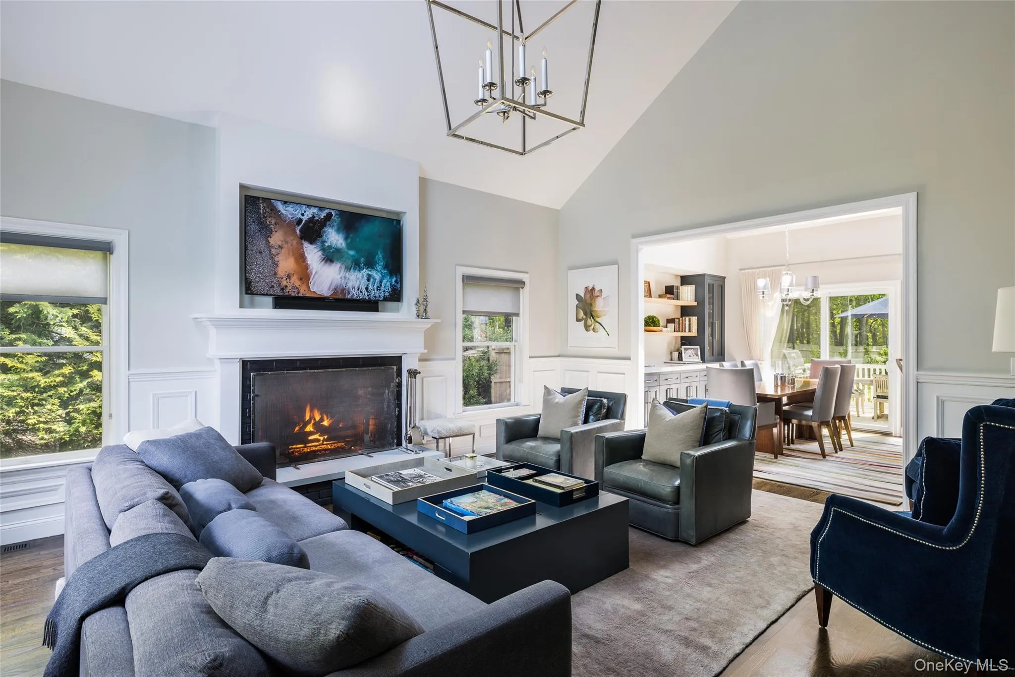 Living area with a chandelier, high vaulted ceiling, a decorative wall, a tiled fireplace, and a wainscoted wall Living area with a chandelier, high vaulted ceiling, a decorative wall, a tiled fireplace, and a wainscoted wall