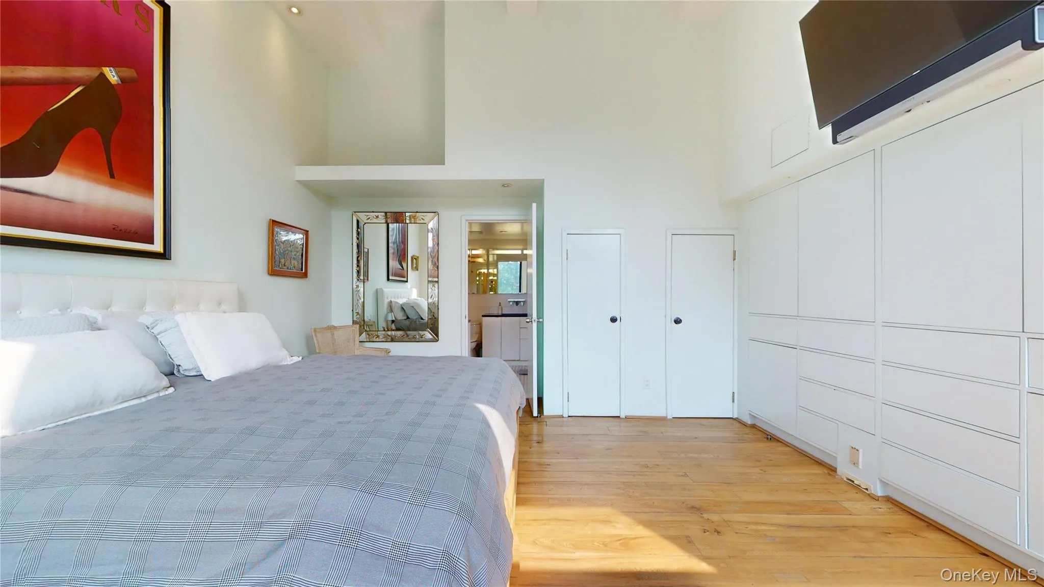 Bedroom featuring light wood-style flooring, a high ceiling, and ensuite bathroom Bedroom featuring light wood-style flooring, a high ceiling, and ensuite bathroom