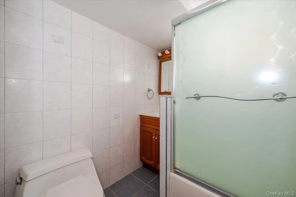 Bathroom featuring vanity, tile walls, bath / shower combo with glass door, and dark tile patterned flooring Bathroom featuring vanity, tile walls, bath / shower combo with glass door, and dark tile patterned flooring