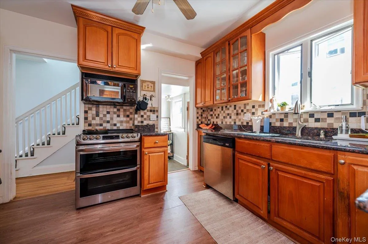Kitchen featuring stainless steel appliances, brown cabinetry, dark stone countertops, and tasteful backsplash Kitchen featuring stainless steel appliances, brown cabinetry, dark stone countertops, and tasteful backsplash