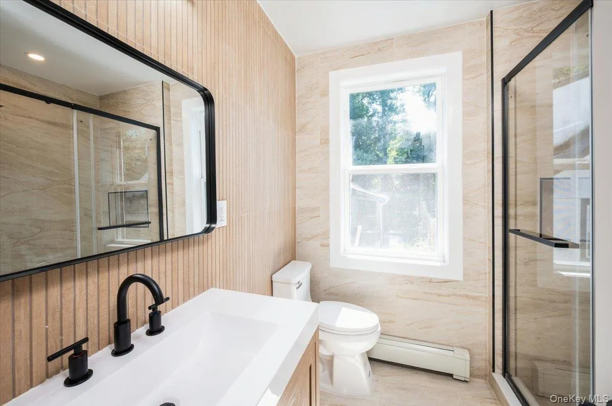Full bath featuring baseboard heating, vanity, a shower stall, and tile walls Full bath featuring baseboard heating, vanity, a shower stall, and tile walls