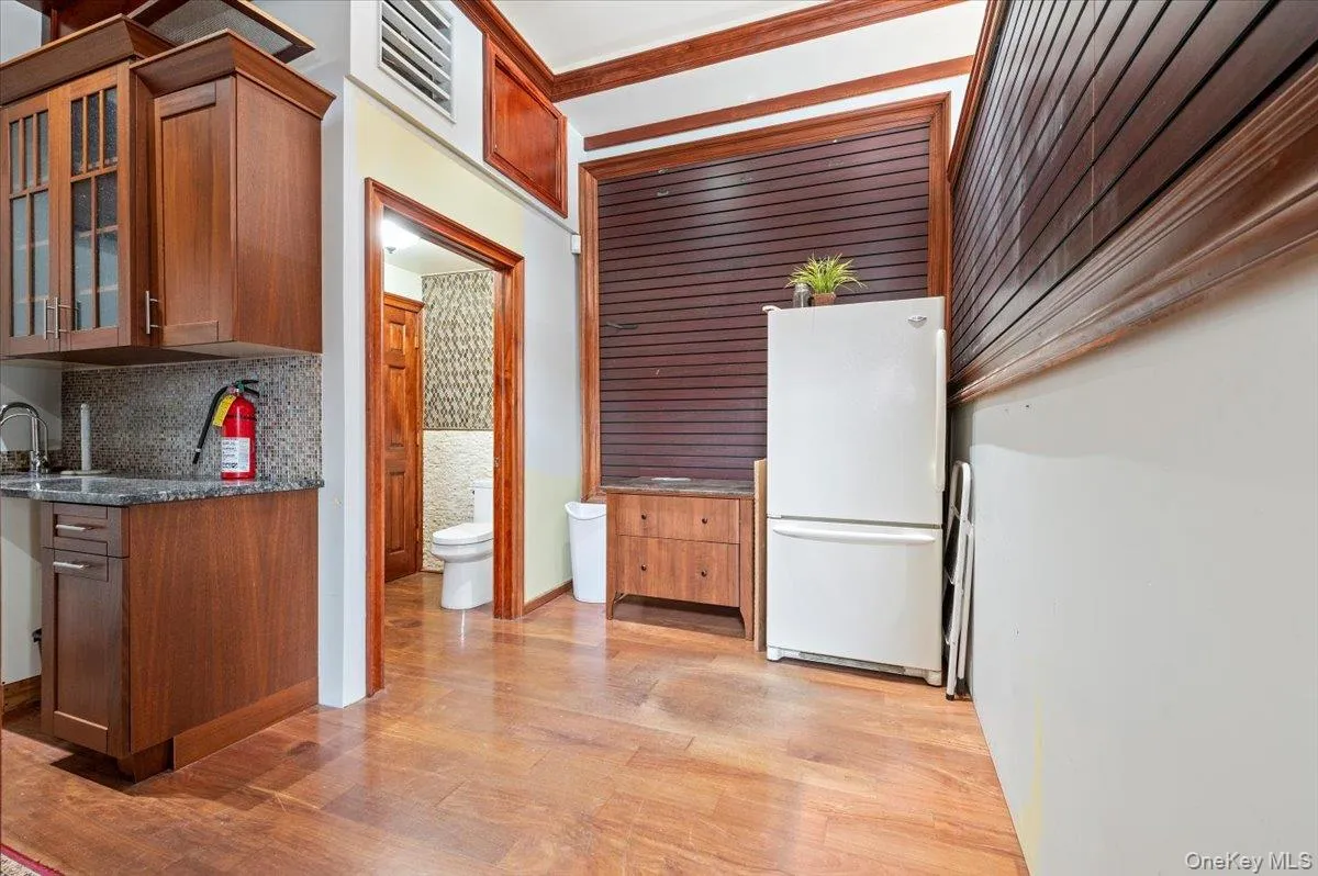 Kitchen with freestanding refrigerator, brown cabinetry, glass insert cabinets, backsplash, and light wood finished floors Kitchen with freestanding refrigerator, brown cabinetry, glass insert cabinets, backsplash, and light wood finished floors