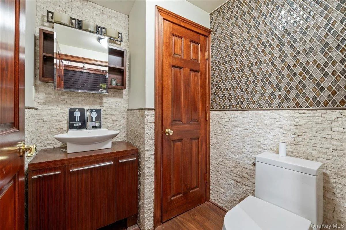 Bathroom with vanity, dark wood-style floors, tile walls, and a wainscoted wall Bathroom with vanity, dark wood-style floors, tile walls, and a wainscoted wall