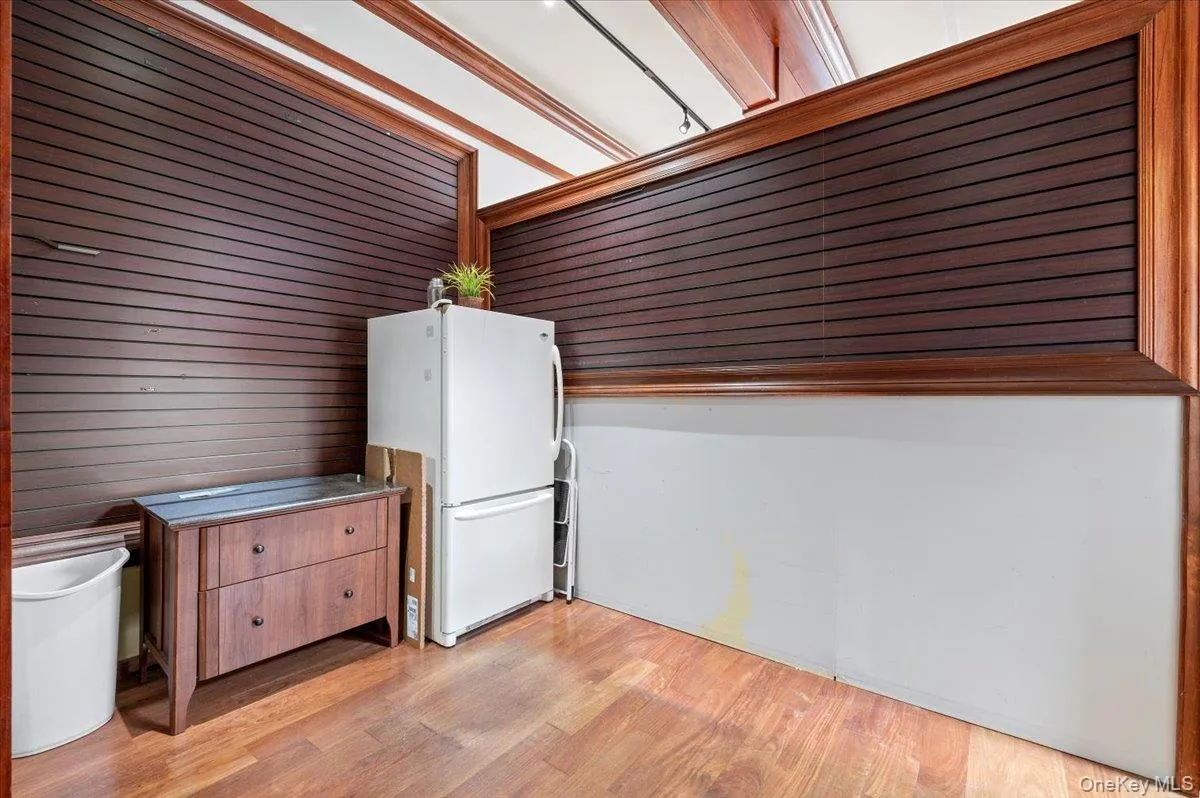 Kitchen with freestanding refrigerator, light wood-style floors, brown cabinetry, and wooden walls Kitchen with freestanding refrigerator, light wood-style floors, brown cabinetry, and wooden walls