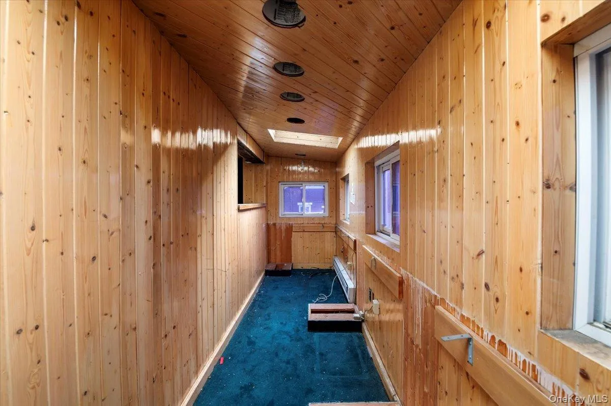 Hallway with wooden walls, dark carpet, and wooden ceiling Hallway with wooden walls, dark carpet, and wooden ceiling