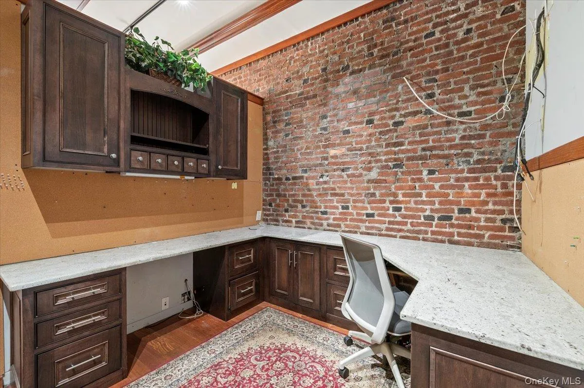 Office area with built in desk, wood finished floors, and brick wall Office area with built in desk, wood finished floors, and brick wall