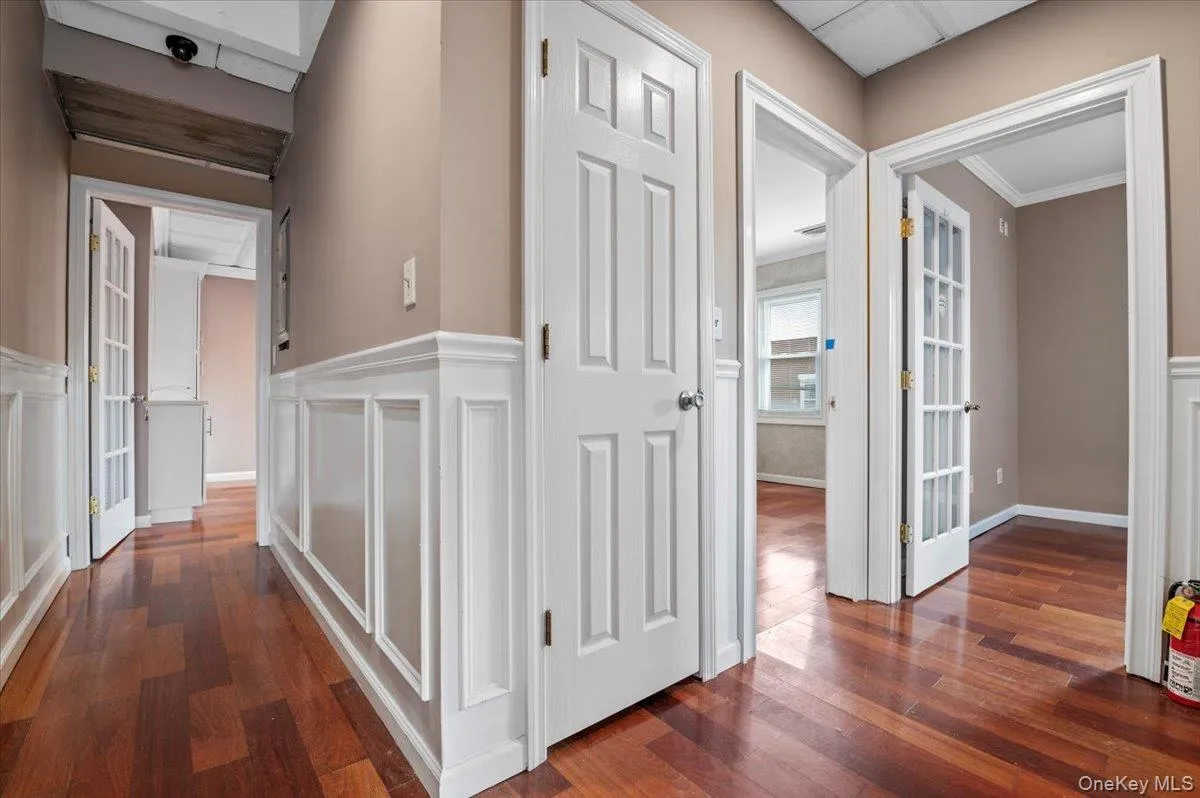 Corridor with dark wood finished floors, a decorative wall, wainscoting, and french doors Corridor with dark wood finished floors, a decorative wall, wainscoting, and french doors