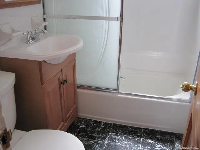 Full bath featuring bath / shower combo with glass door, vanity, and dark marble finish floors Full bath featuring bath / shower combo with glass door, vanity, and dark marble finish floors