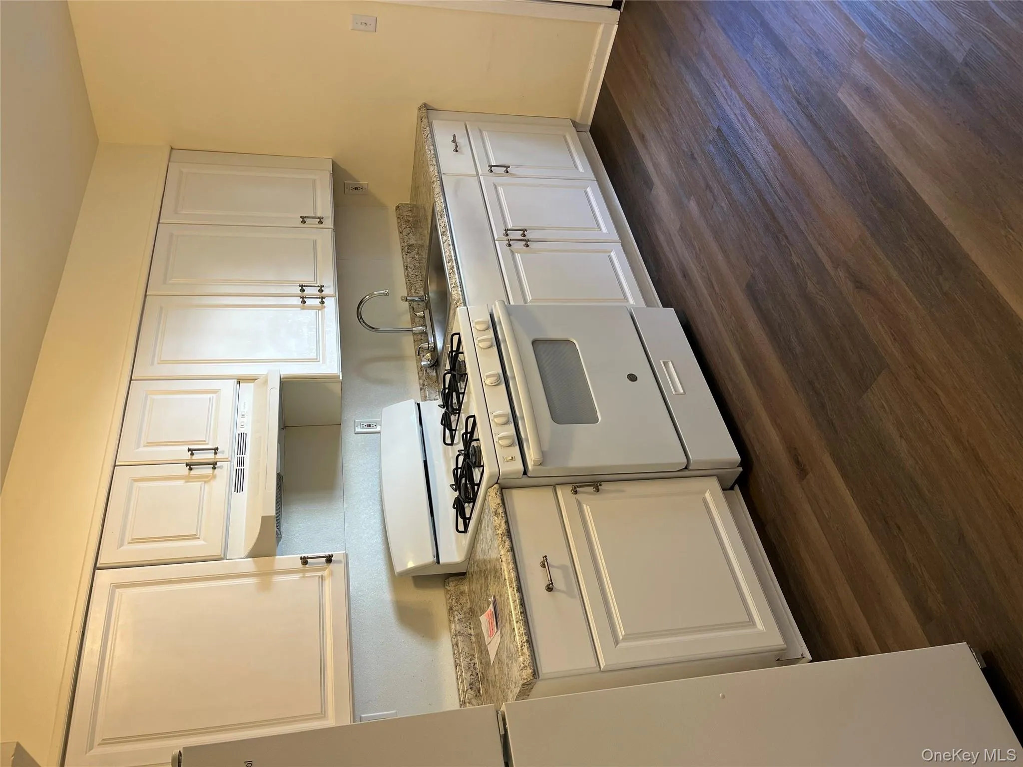 Kitchen featuring white range with gas stovetop, white cabinets, paneled fridge, and dark wood-style flooring Kitchen featuring white range with gas stovetop, white cabinets, paneled fridge, and dark wood-style flooring