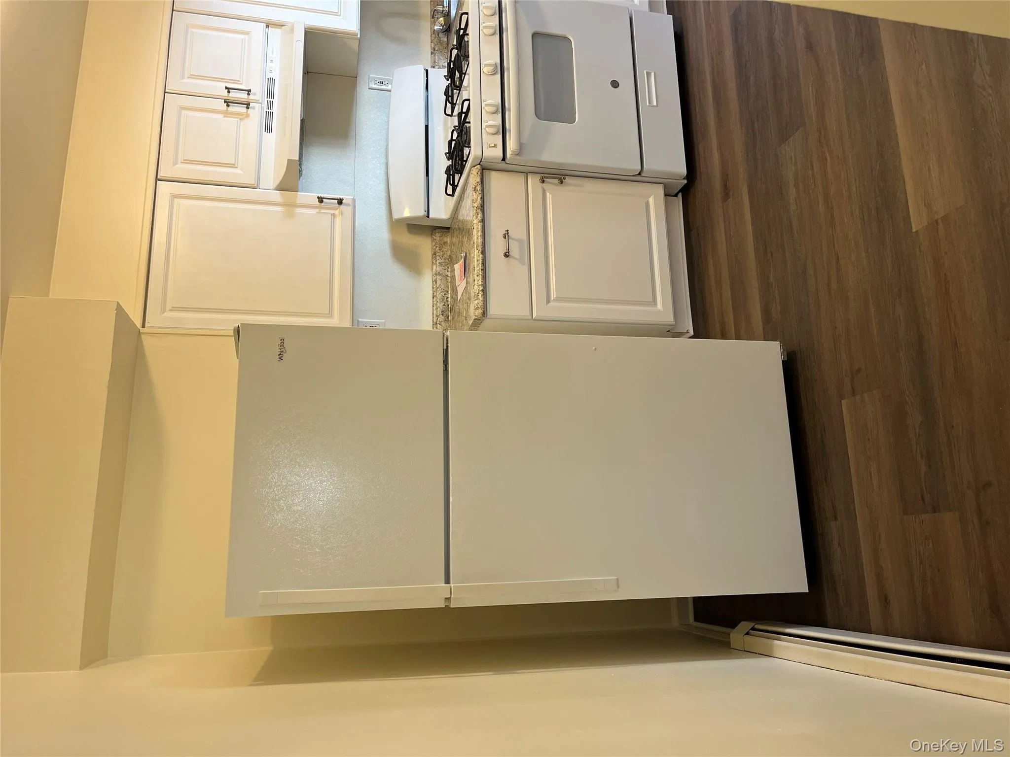 Kitchen with freestanding refrigerator, range, white cabinets, light countertops, and baseboard heating Kitchen with freestanding refrigerator, range, white cabinets, light countertops, and baseboard heating