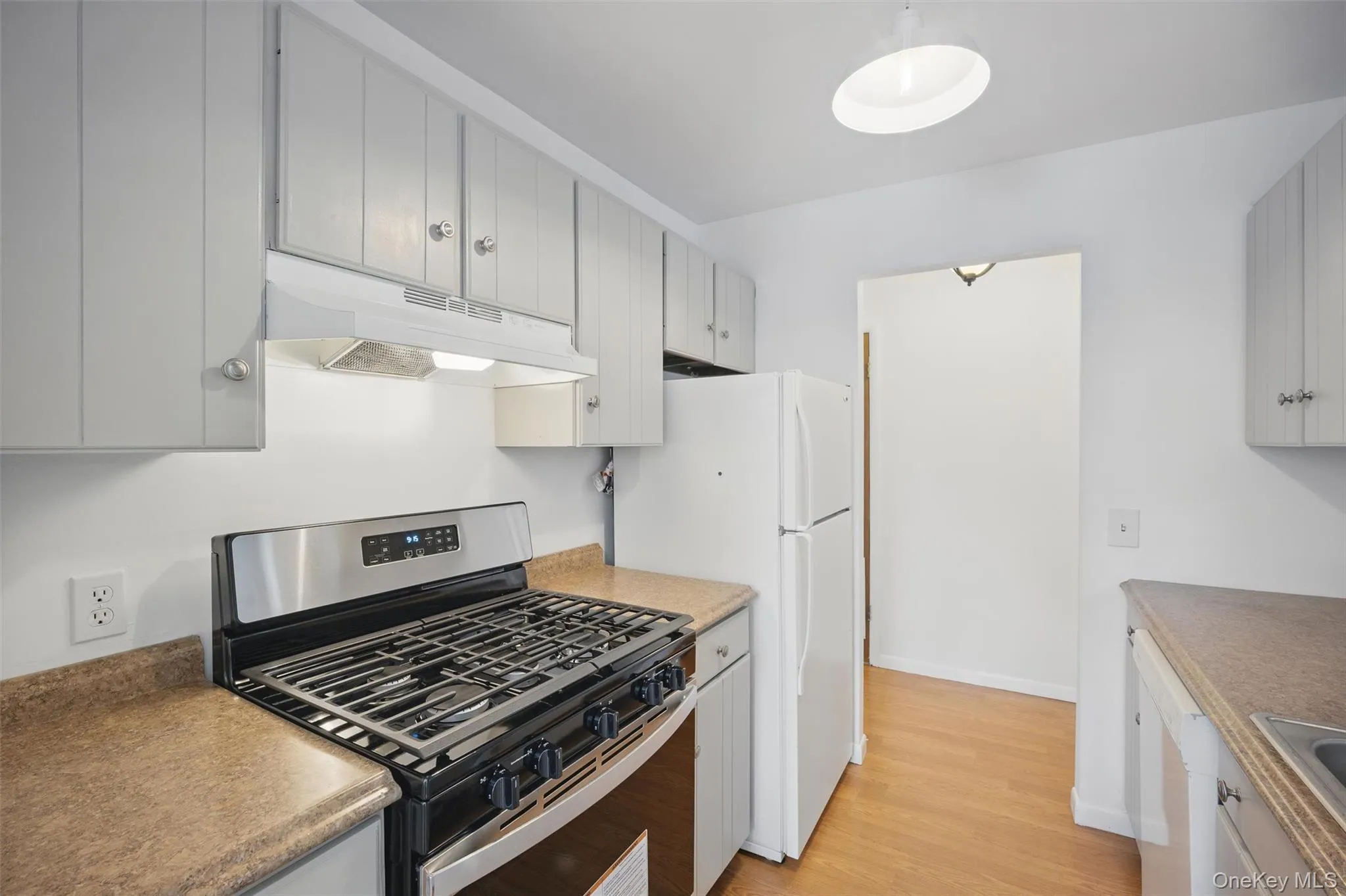 Kitchen featuring white appliances, under cabinet range hood, light wood-type flooring, and gray cabinets Kitchen featuring white appliances, under cabinet range hood, light wood-type flooring, and gray cabinets