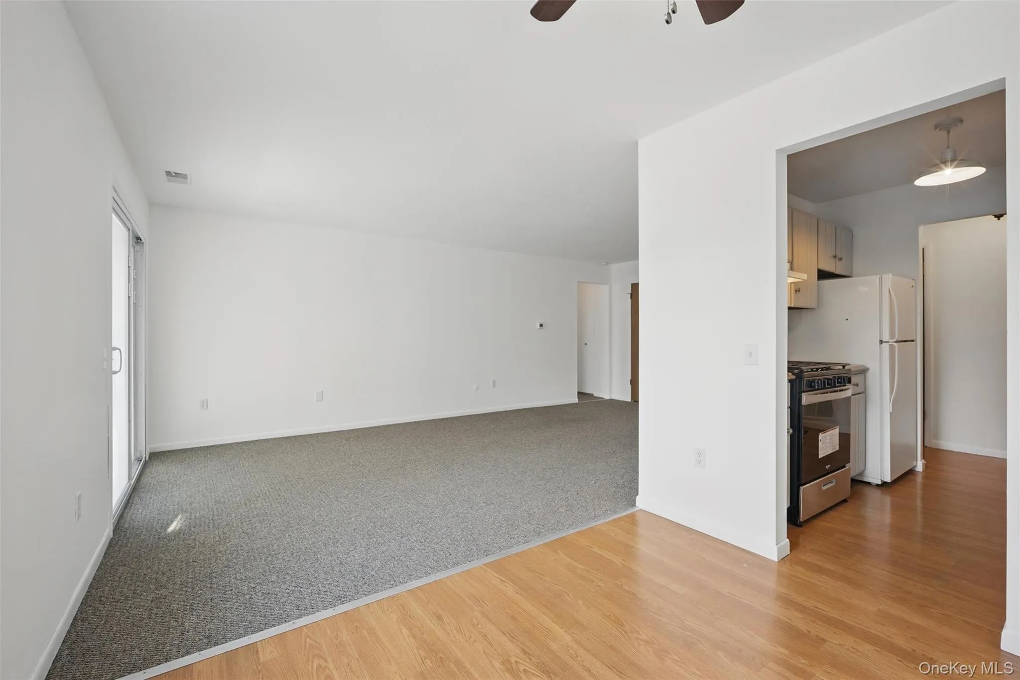Unfurnished living room with light wood finished floors, ceiling fan, and light colored carpet Unfurnished living room with light wood finished floors, ceiling fan, and light colored carpet