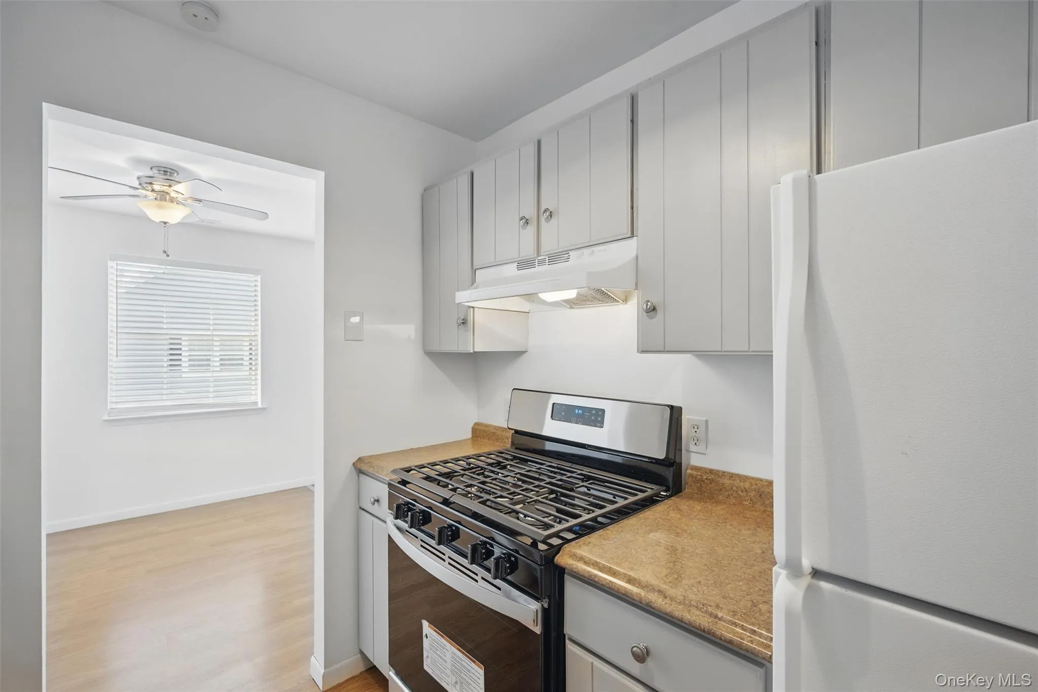 Kitchen featuring gas range, freestanding refrigerator, light wood-style floors, under cabinet range hood, and a ceiling fan Kitchen featuring gas range, freestanding refrigerator, light wood-style floors, under cabinet range hood, and a ceiling fan