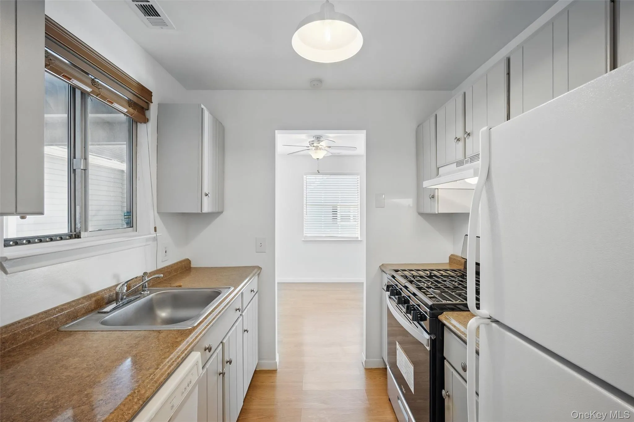 Kitchen featuring white appliances, light wood-type flooring, under cabinet range hood, a ceiling fan, and white cabinets Kitchen featuring white appliances, light wood-type flooring, under cabinet range hood, a ceiling fan, and white cabinets