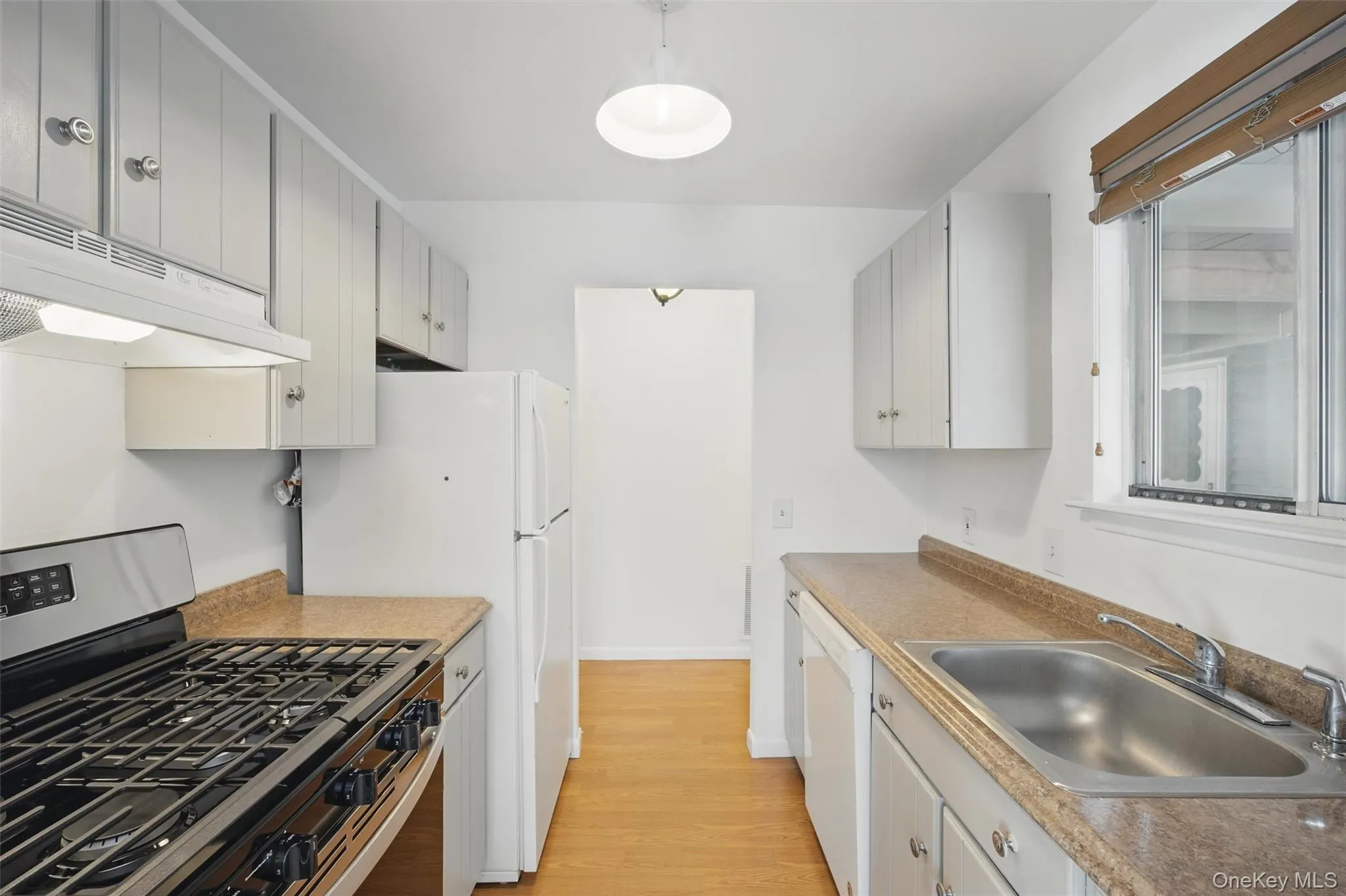 Kitchen with white appliances, light wood-style flooring, under cabinet range hood, and light countertops Kitchen with white appliances, light wood-style flooring, under cabinet range hood, and light countertops