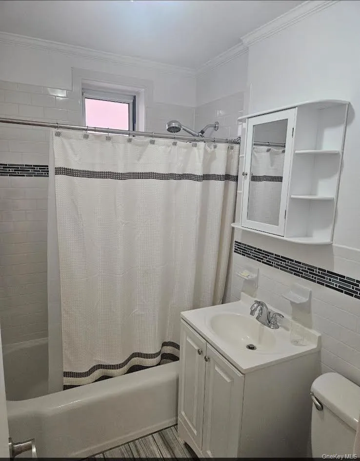 Bathroom featuring shower / tub combo with curtain, tile walls, crown molding, and vanity Bathroom featuring shower / tub combo with curtain, tile walls, crown molding, and vanity