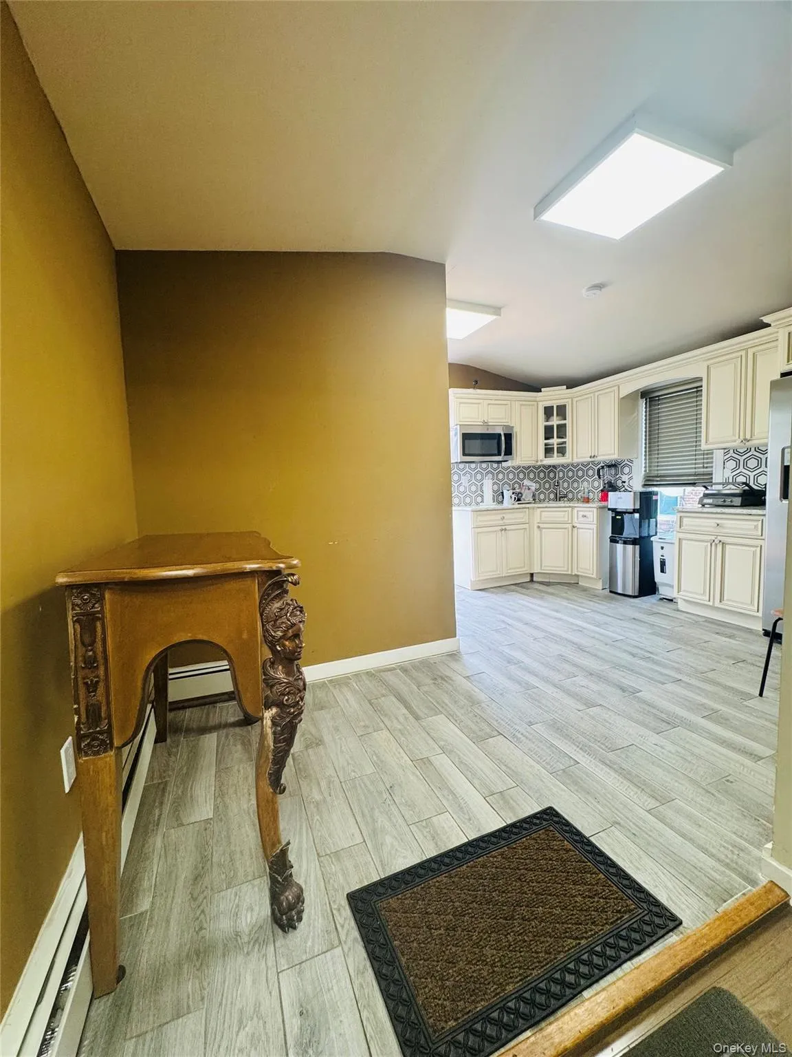 Kitchen with glass insert cabinets, backsplash, light wood finished floors, and a baseboard heating unit Kitchen with glass insert cabinets, backsplash, light wood finished floors, and a baseboard heating unit