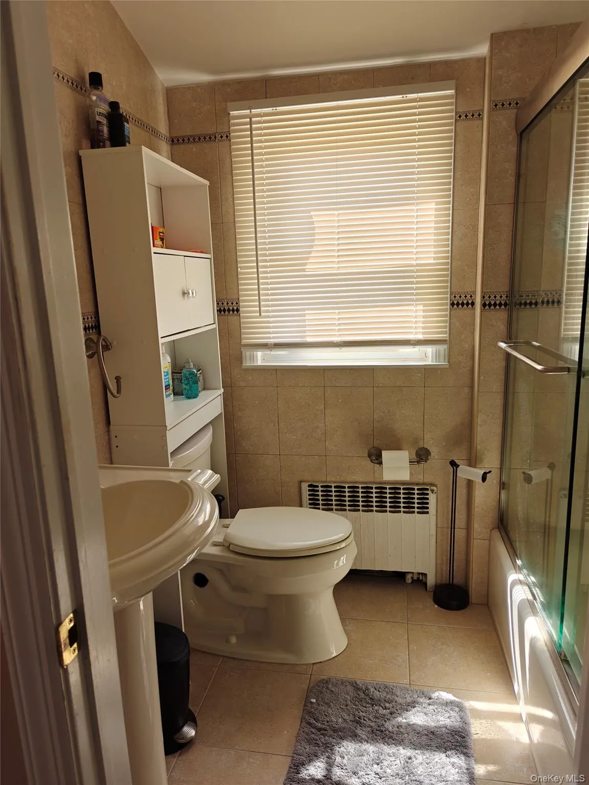 Full bathroom with tile walls, enclosed tub / shower combo, radiator, and light tile patterned floors Full bathroom with tile walls, enclosed tub / shower combo, radiator, and light tile patterned floors