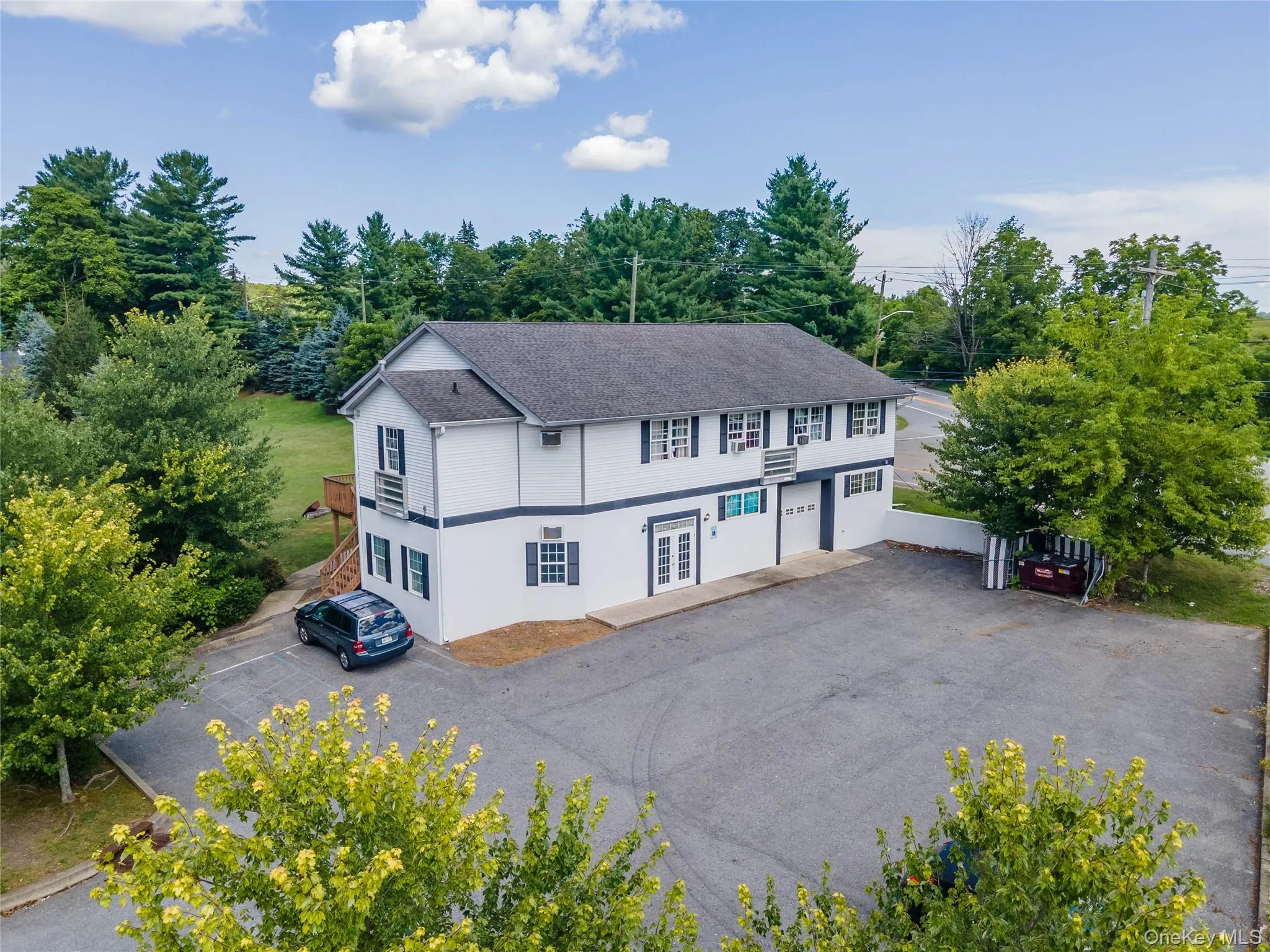 View of front of home with a shingled roof, french doors, view of scattered trees, and asphalt driveway View of front of home with a shingled roof, french doors, view of scattered trees, and asphalt driveway