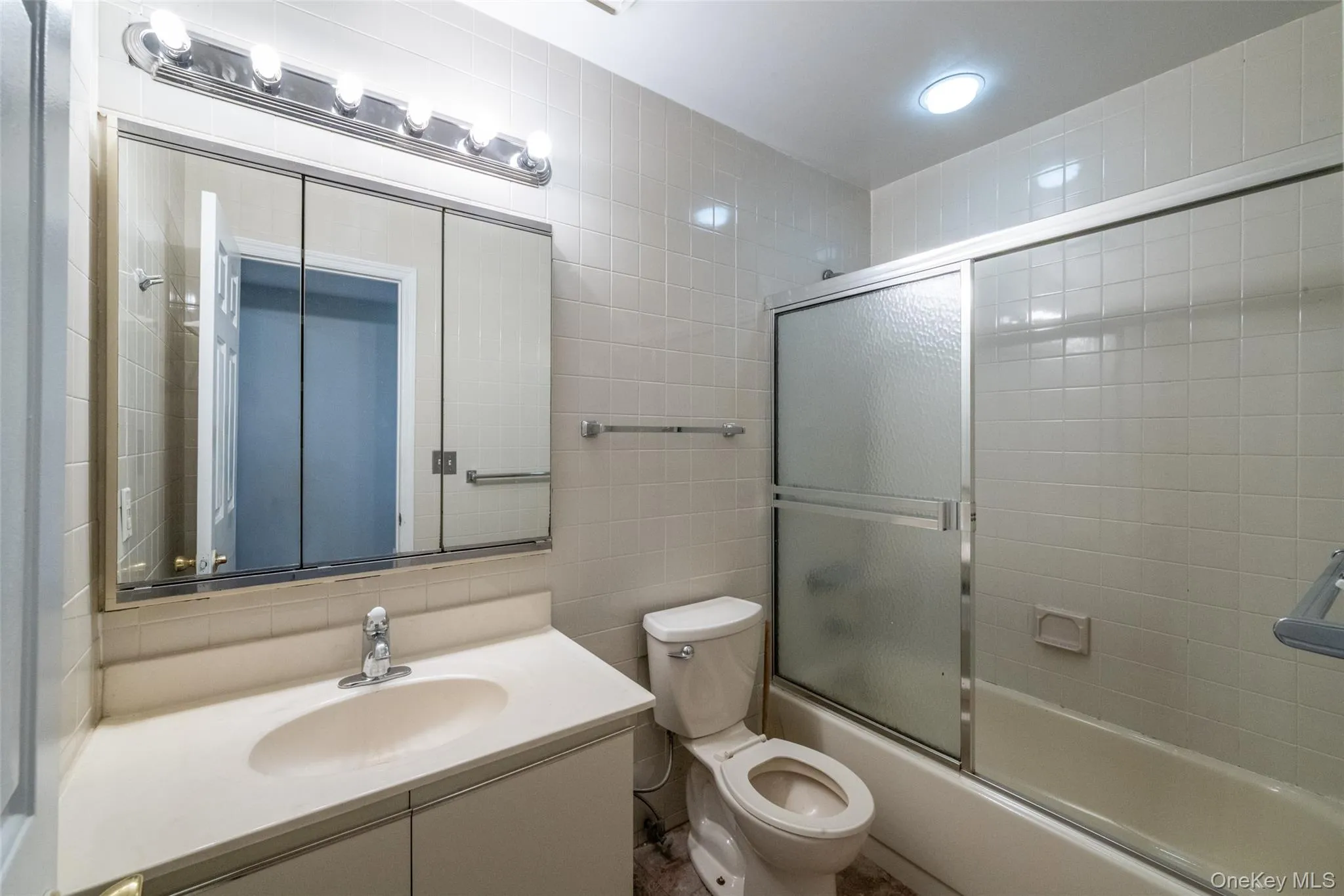 Hall Full bathroom with tile walls, vanity, bath / shower combo with glass door Hall Full bathroom with tile walls, vanity, bath / shower combo with glass door