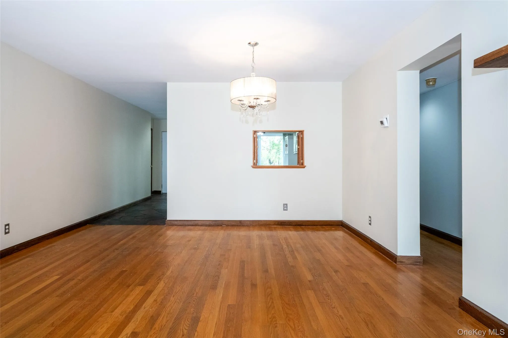 Empty room with a chandelier and dark wood-style flooring Empty room with a chandelier and dark wood-style flooring