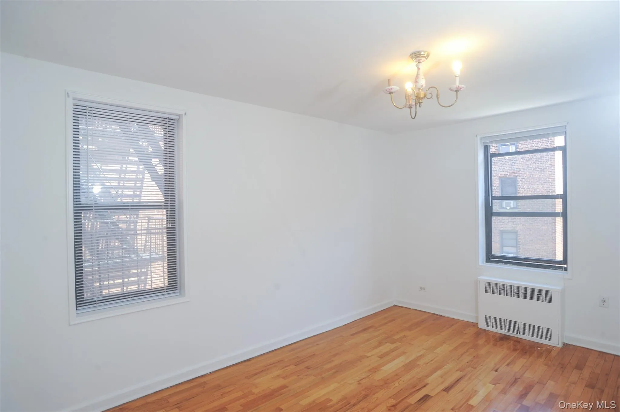 Unfurnished room with light wood-style flooring, radiator heating unit, and a chandelier Unfurnished room with light wood-style flooring, radiator heating unit, and a chandelier