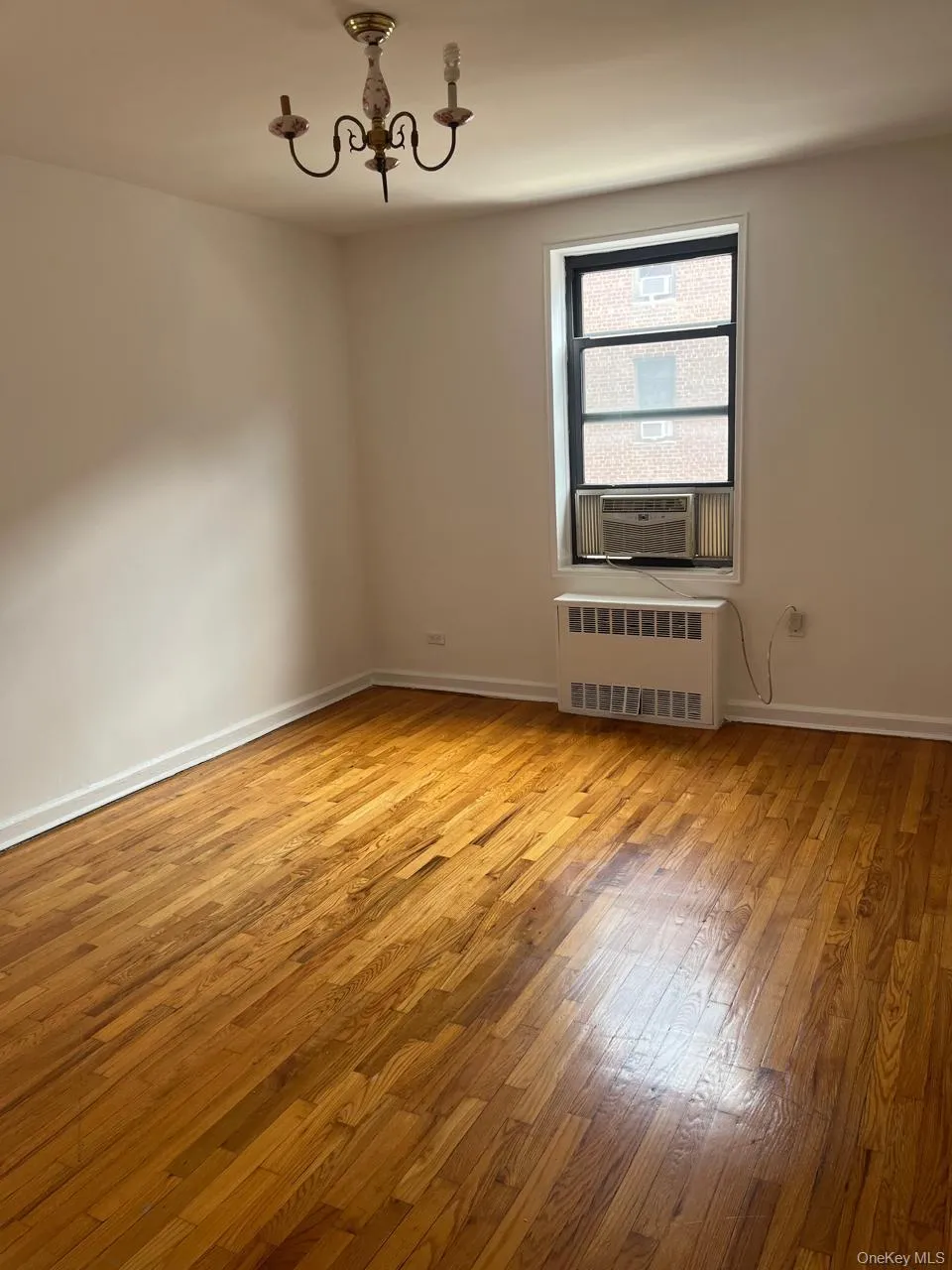 Empty room featuring light wood-type flooring, radiator, and a chandelier Empty room featuring light wood-type flooring, radiator, and a chandelier