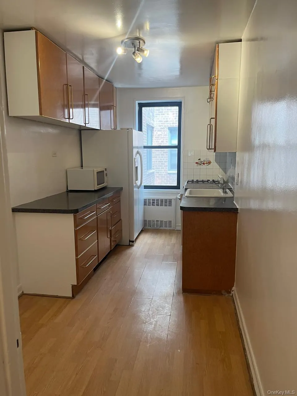 Kitchen with dark countertops, brown cabinetry, light wood-style floors, radiator, and white microwave Kitchen with dark countertops, brown cabinetry, light wood-style floors, radiator, and white microwave
